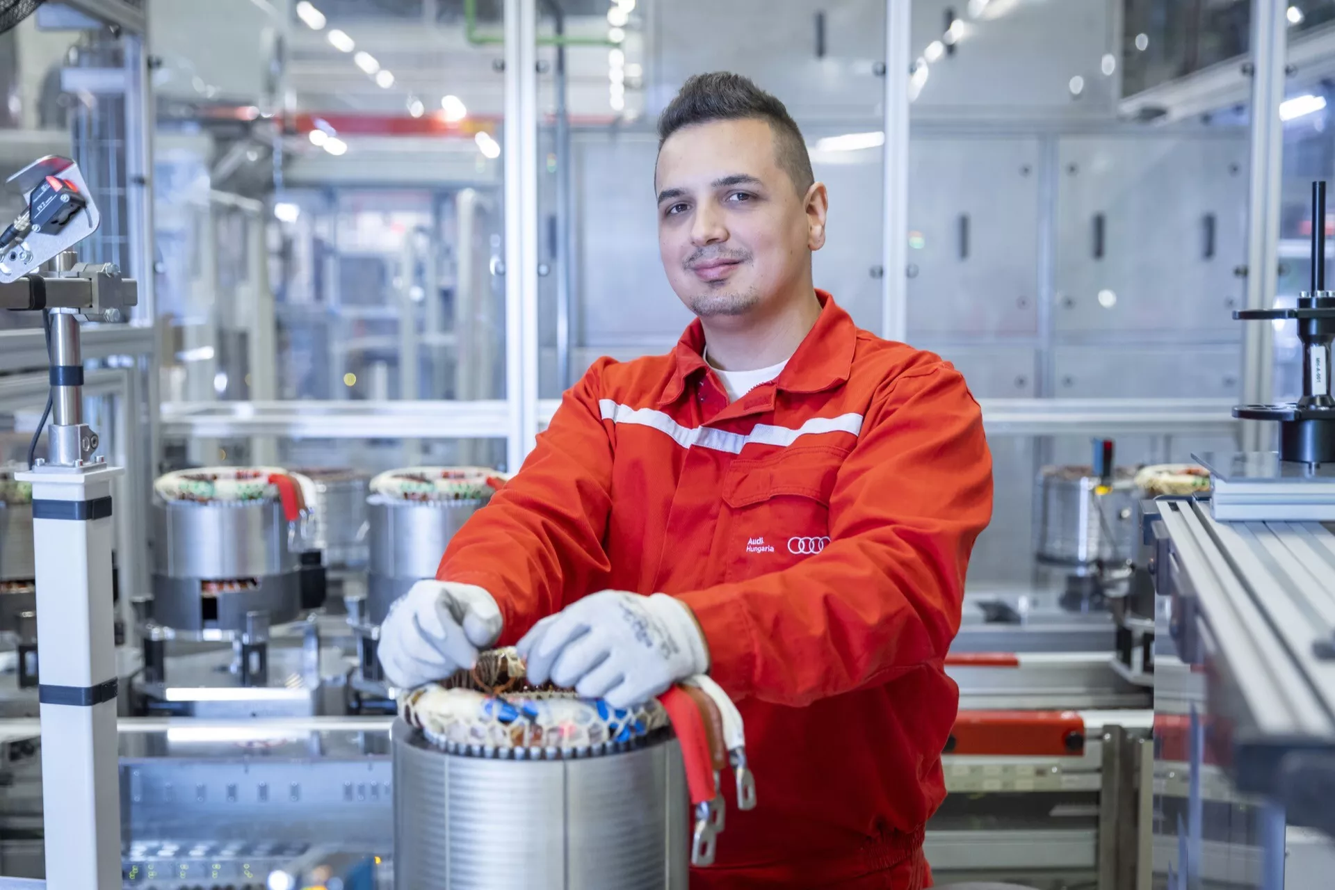 Strokovnjak za avtomobilsko inženirstvo v rdeči uniformi dela na komponenti električnega pogona v sodobnem proizvodnem obratu