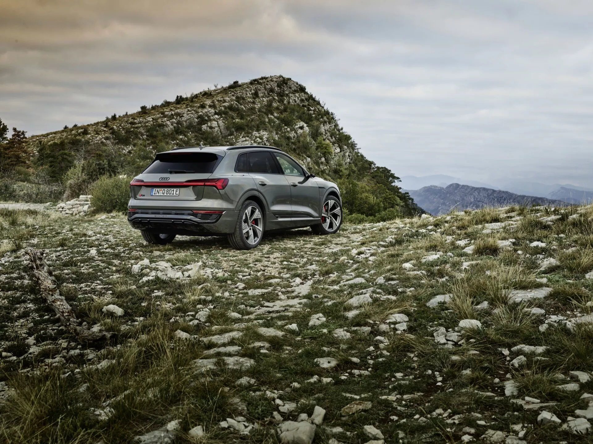 Audi Q8 e-tron 2023 z metalnim zaključkom, postavljen na robustnem zunanjem terenu, ki prikazuje terenske zmogljivosti, športno in praktično obliko z LED zadnjimi lučmi, lita platišča in naprednimi tehnološkimi lastnostmi
