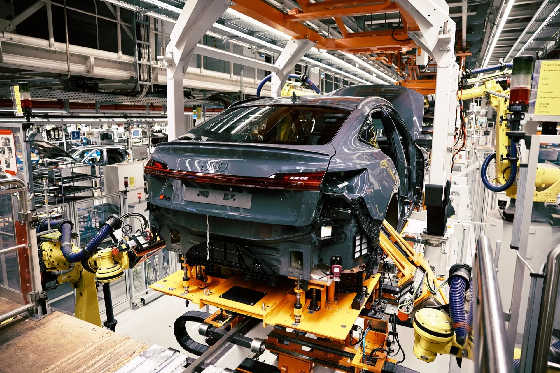 Audi Q8 e-tron 2023 v proizvodnji, pogled od zadaj treh četrtin, ki prikazuje LED zadnje luči in visoko sijajno finiširanje na montažni liniji