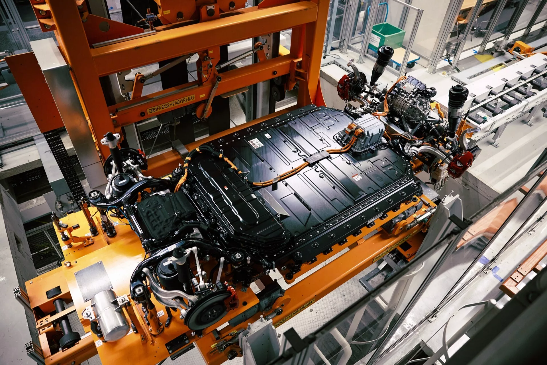 Pogled od zgoraj na spodnji del Audi Q8 e-tron 2023 med sestavljanjem, ki prikazuje šasijo, velik električni baterijski paket in vzmetenje v tovarniškem okolju