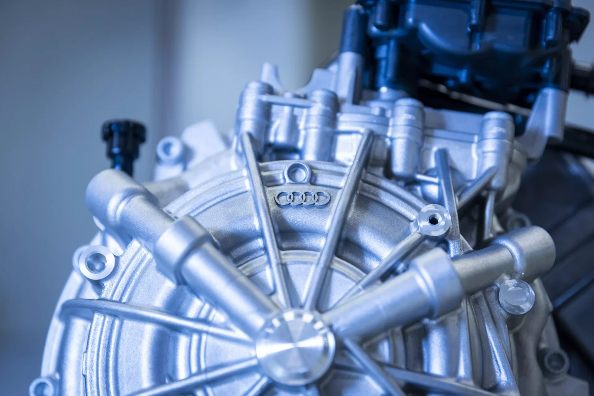 Podroben pogled na komponento motorja Audi Q8 e-tron 2023, s prikazom krožnega središča z radialnimi elementi in logotipom Audi, ki prikazuje napredno avtomobilsko inženirstvo in natančno izdelavo.