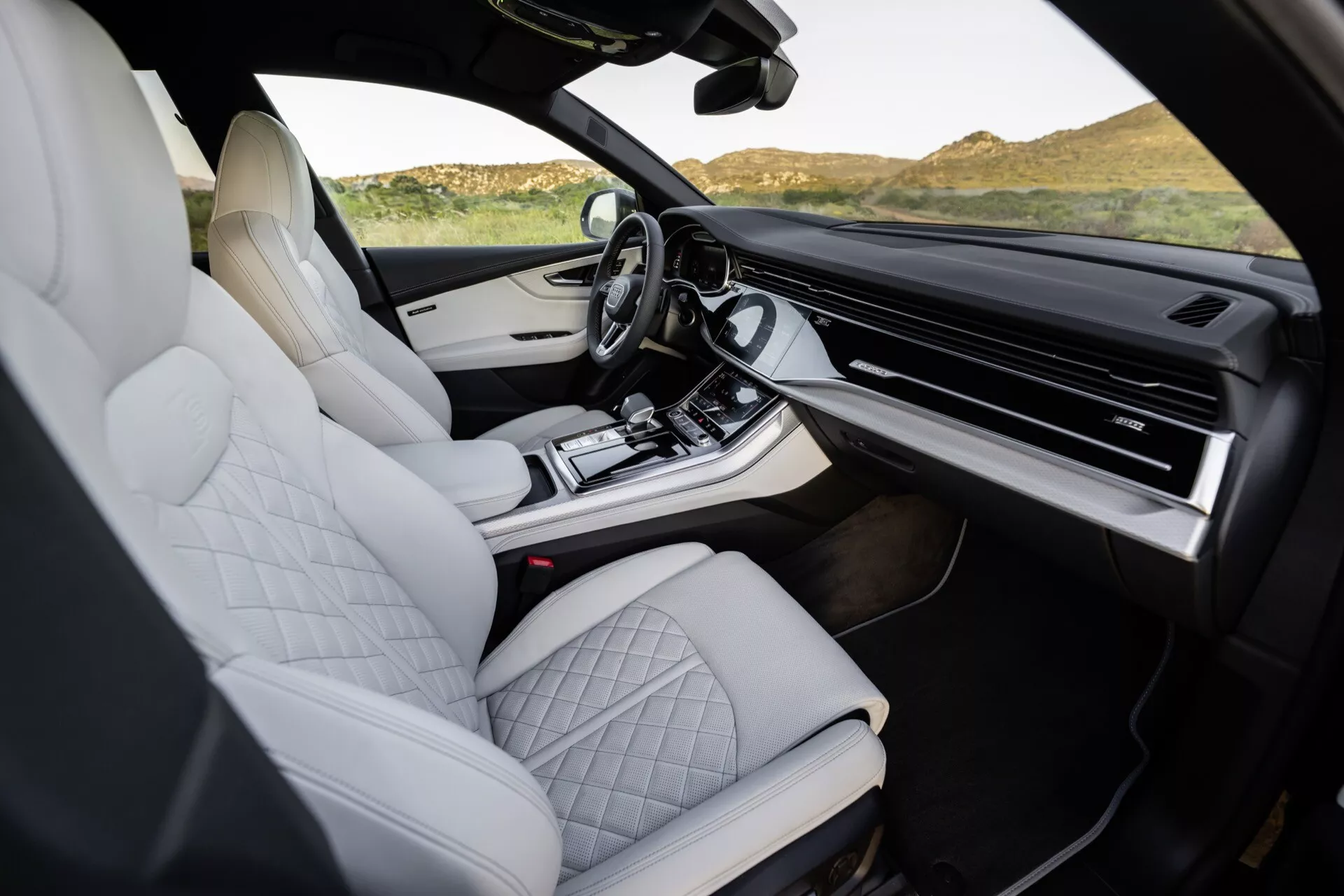Notranjost Audi Q8 2023 (4M-Facelift), ki prikazuje bele prešite usnjene sedeže, vrhunsko zasnovo srednje konzole, obsežen zaslon na dotik za informacijsko-zabavni sistem in sodobne, ergonomske funkcije, posneto iz perspektive sopotnika