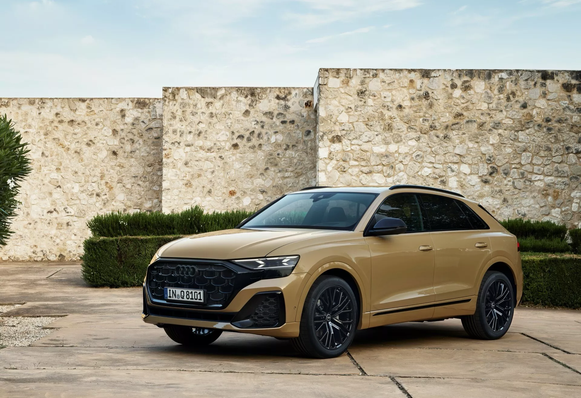 Moderno SUV vozilo Audi Q8 2023 (4M-Facelift) v umirjeno zlati barvi, parkirano na zgodovinskem dvorišču, ki prikazuje sprednji žar, elegantne žaromete in športni stranski profil z tehnološkimi lastnostmi in elementi luksuzne zasnove v naravni svetlobi