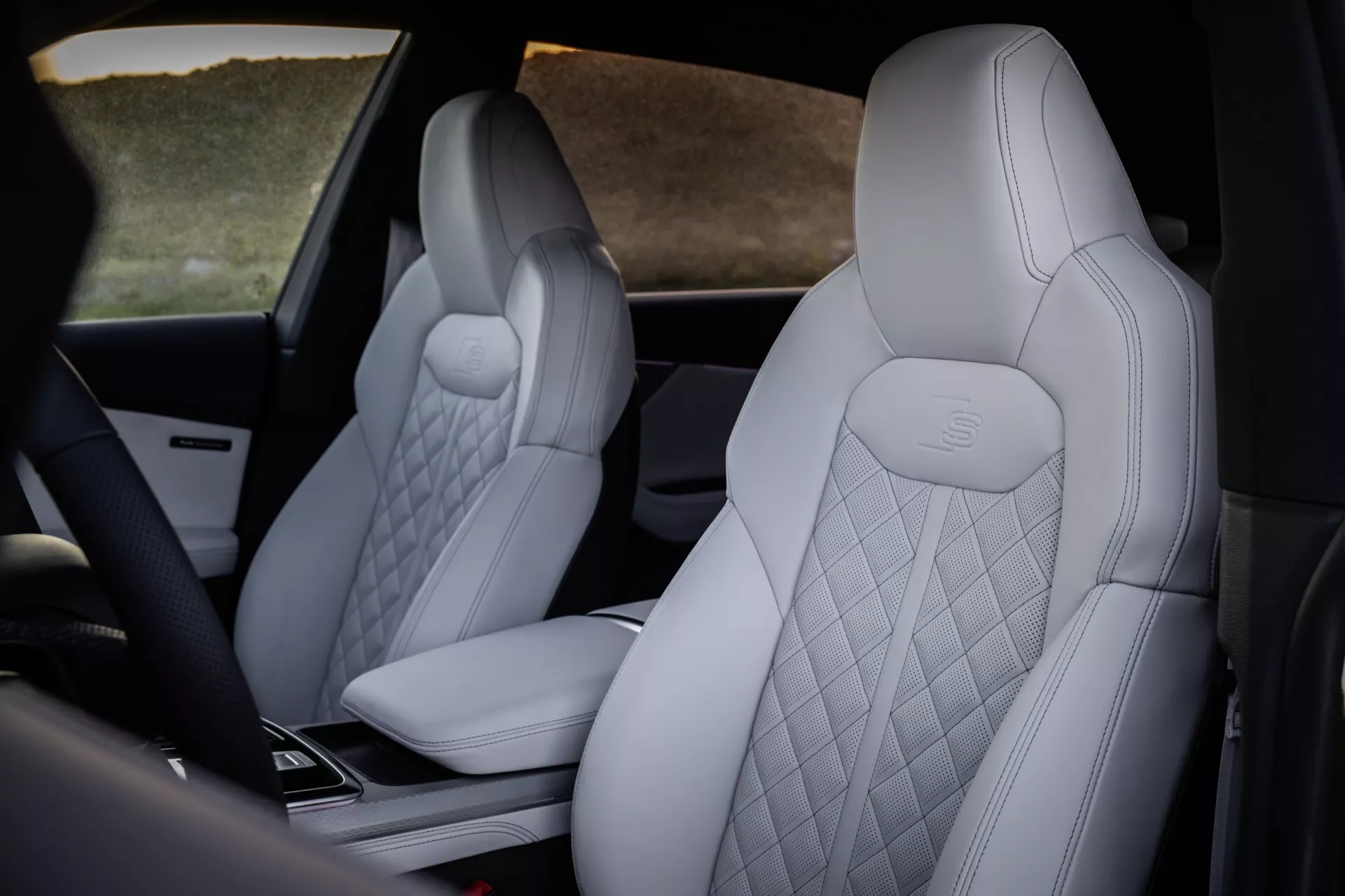 Notranjost Audi Q8 2023 (4M-Facelift), ki poudarja razkošne sprednje sedeže z lahko, diamantno šivano oblazinjenje in reliefnim logotipom Mercedes-Benz, z delnim pogledom na visokotehnološko sredinsko konzolo iz perspektive zadaj in malo postrani.