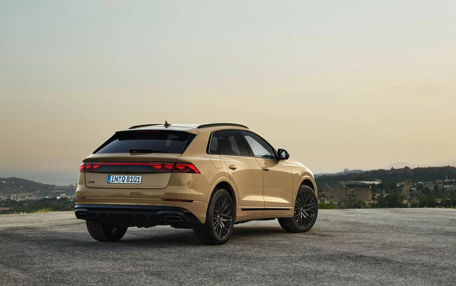 Audi Q8 2023 (4M-Facelift) v kovinski barvi, parkiran na razgledni točki s hribi in nebo ob zori/mraku, prikazan z zadnjega kota treh četrtin za ogled oblike in funkcij