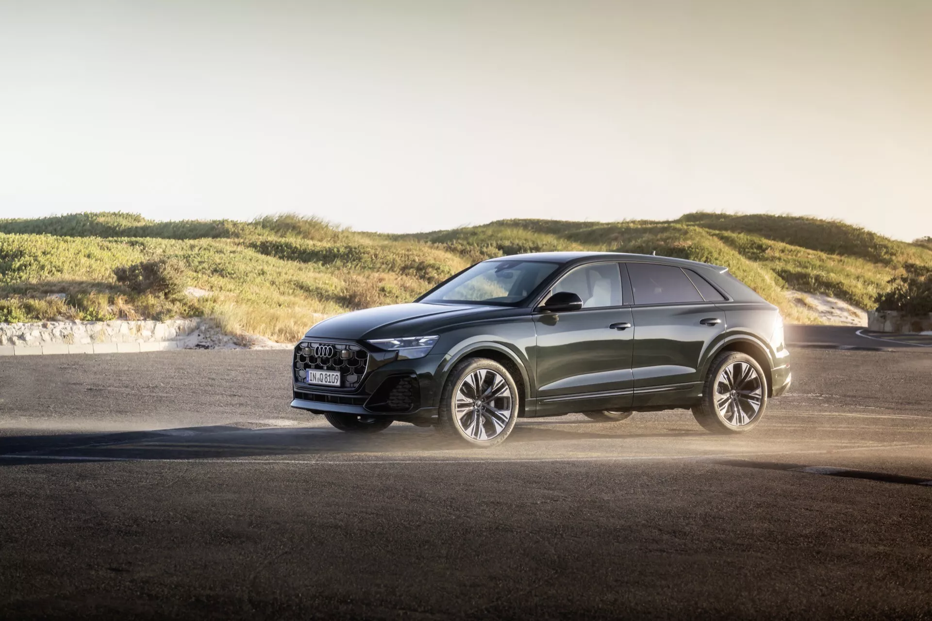 Moderen križanec Audi Q8 2023 (4M-Facelift) na prostem med zlato uro, ki prikazuje napredne LED žaromete, luksuzno rešetko z varnostnimi funkcijami, velika lita kolesa usmerjena na zmogljivost, metalik barvo in športne oblikovalske linije ob asfaltu in mehkih hribih, kar poudarja vsestranske sposobnosti in dizajn