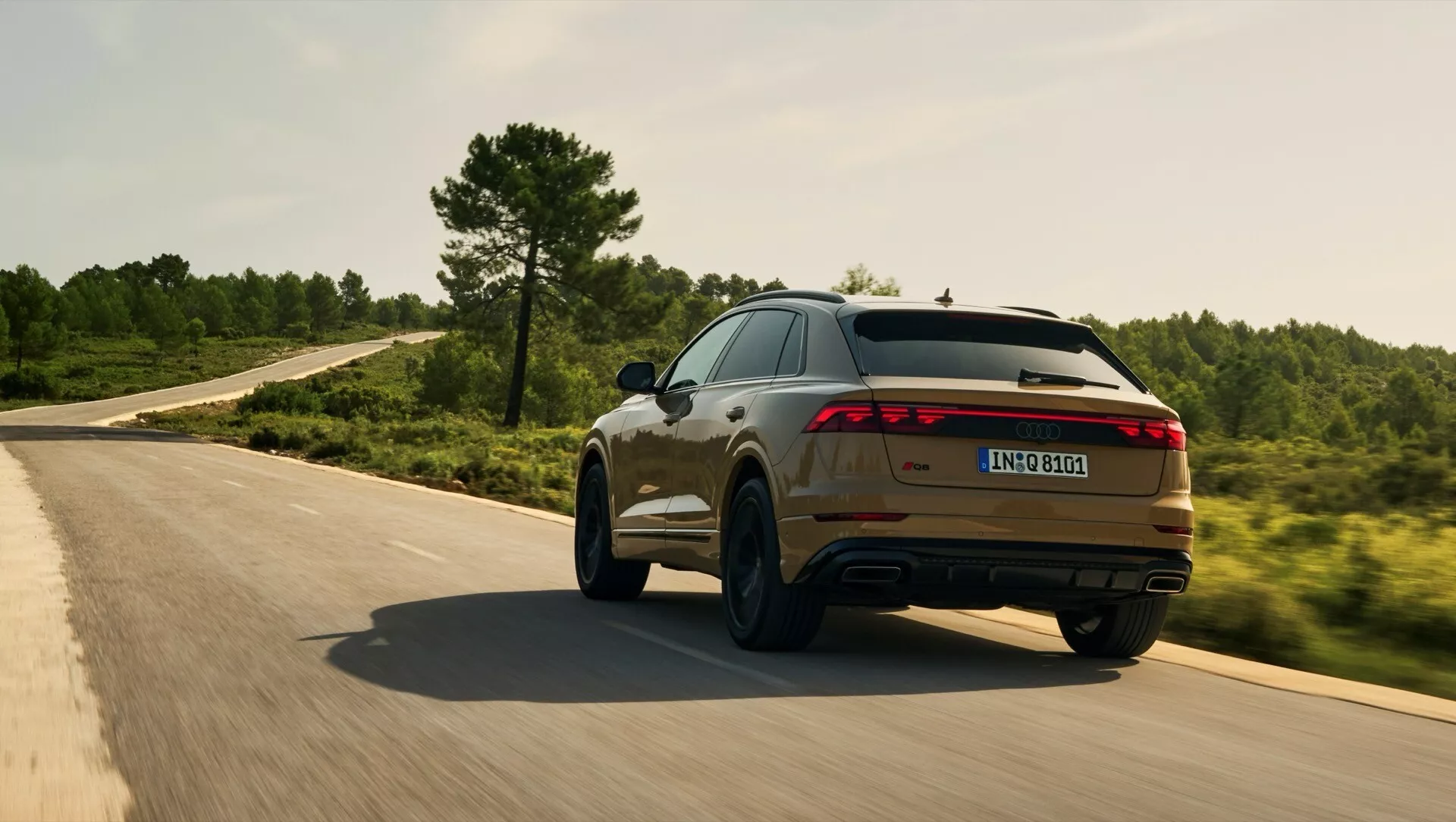 Audi Q8 2023 (4M-Facelift) v gibanju na ovinkasti cesti, prikazuje svoj športni zadnji in stranski profil z LED svetlobno vrstico, dvojnim izpuhom in kovinskim zaključkom