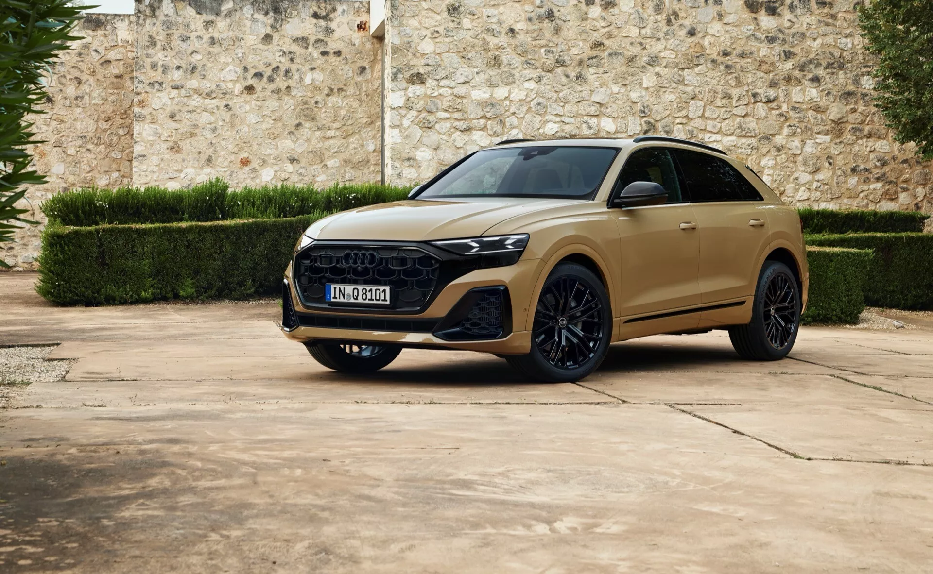 Luksuzni crossover SUV Audi Q8 2023 v pogledu iz treh četrtin od spredaj, parkiran na tlakovci z ozadjem stare kamnite stene, z elegantnimi LED žarometi, izrazito heksagonalno masko, oblikovanimi linijami pokrova, velikimi zlitinskimi kolesi in možno panoramsko streho.