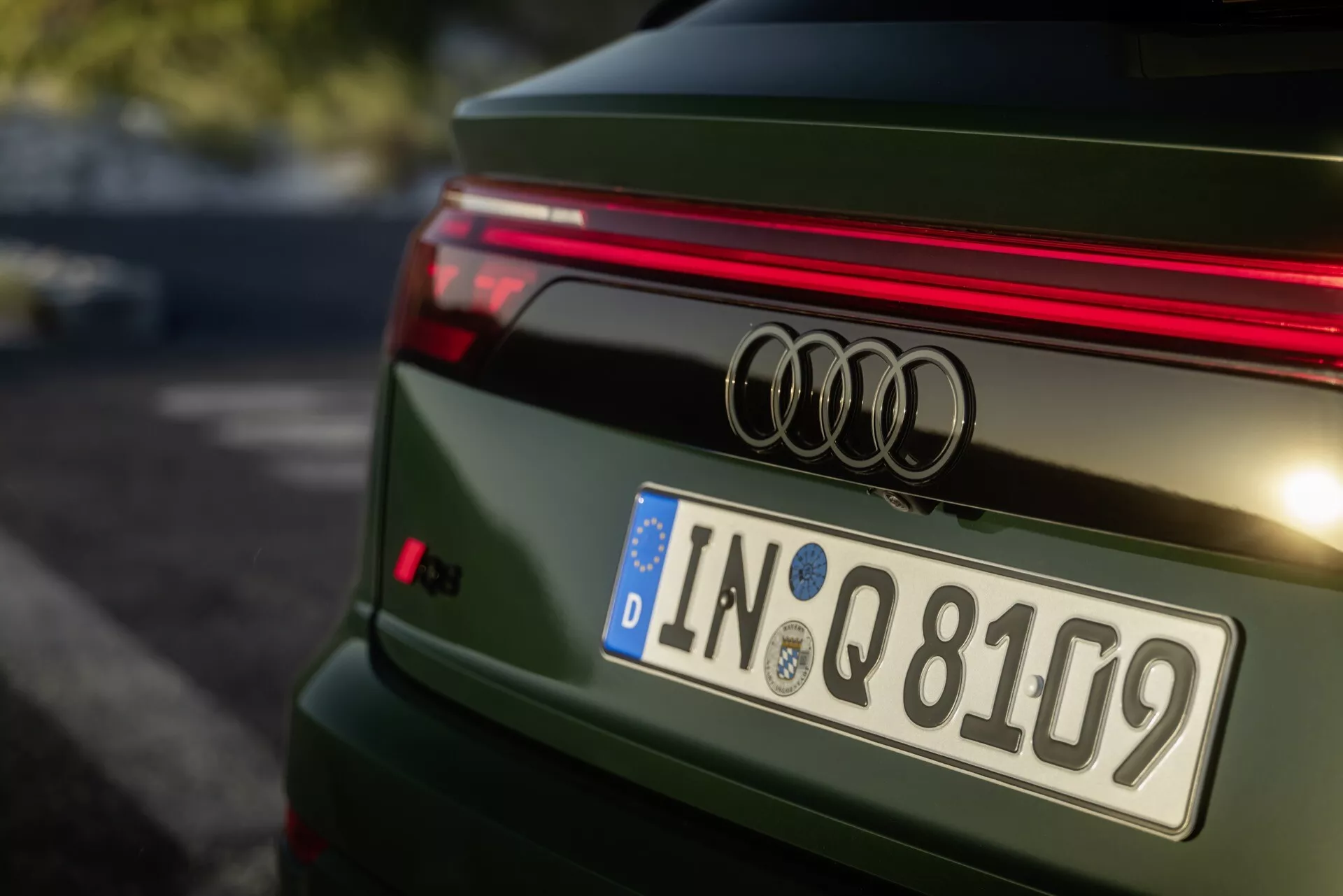 Podroben pogled od zadaj na zeleni Audi Q8 letnik 2023 po prenovi 4M, prikazuje značko Audi, vodoravni LED trak, evropsko registracijsko tablico iz Ingolstadta in športni spojler, z detajlno zasnovanim pokrova prtljažnika in poliranim kovinskim finišem.