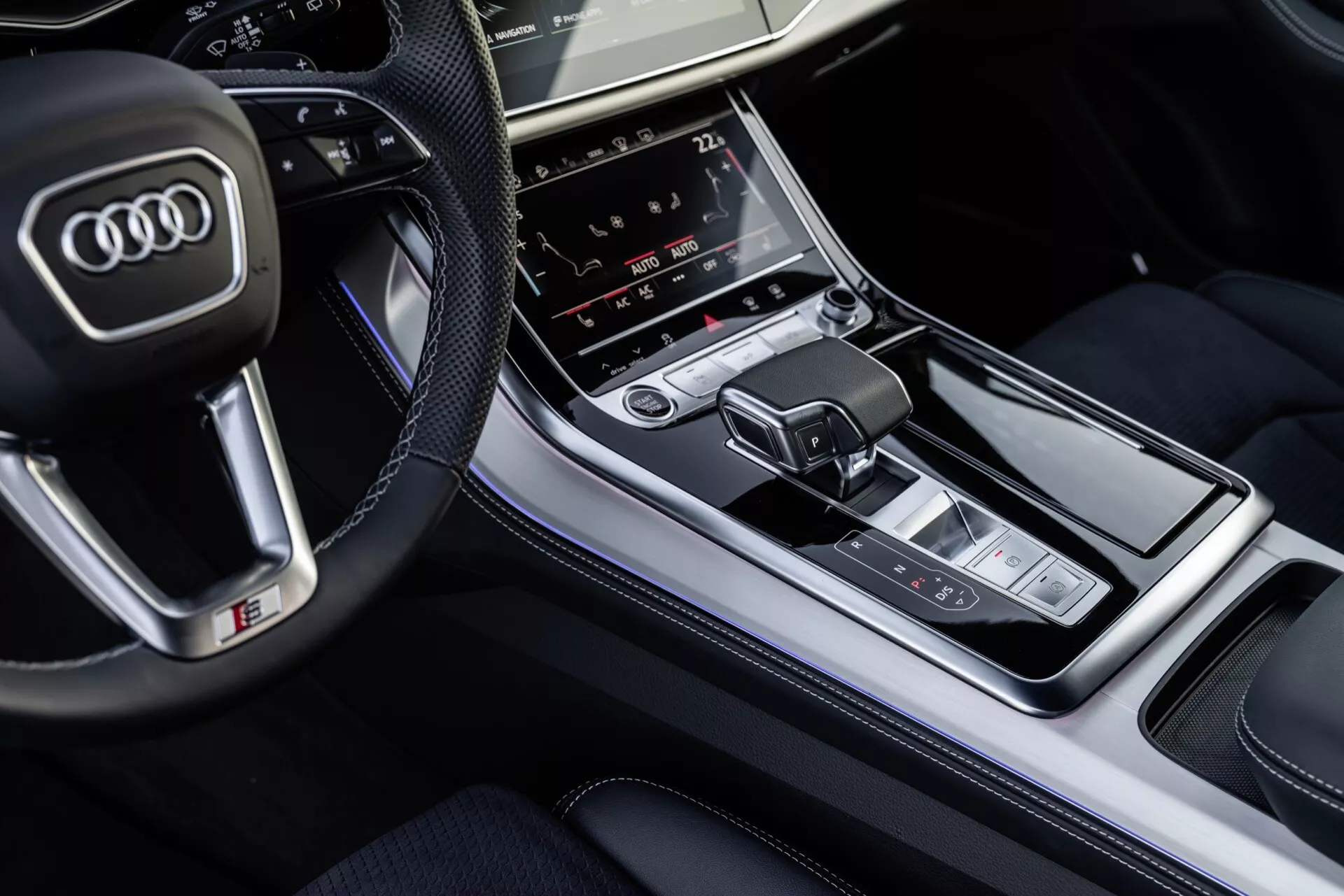 Pogled od zgoraj na notranjost Audi Q8 2023, osredotočen na sredinsko konzolo z izbiro prestav in multimedijskim kontrolnim panelom, ki poudarja luksuzne zaključke in napredne tehnološke funkcije