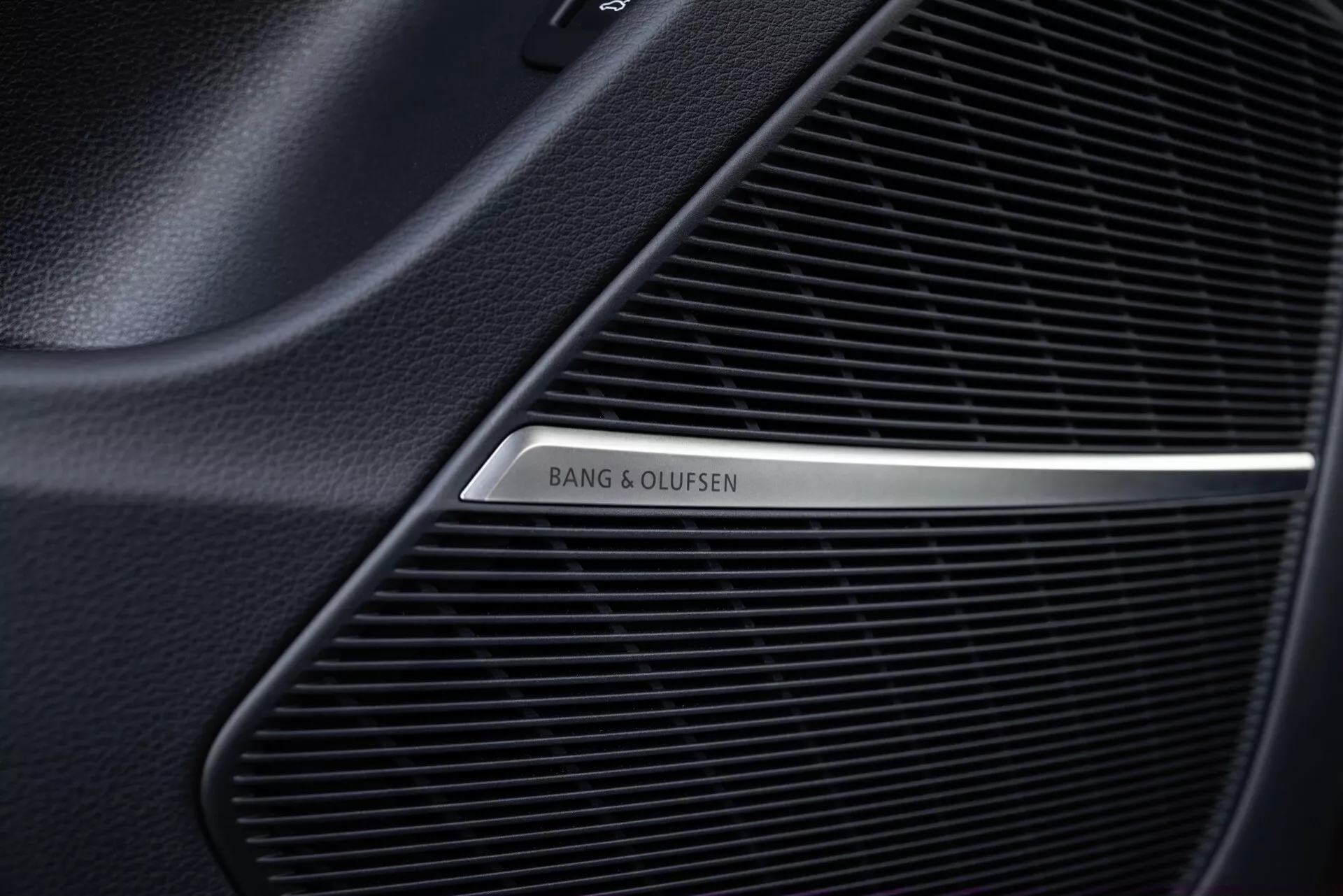 Posnetek iz bližine rešetke zvočnika Bang & Olufsen v notranjosti Audi Q8 2023 (4M-Facelift), ki prikazuje fino mrežasto vzorec vrhunskega avdio sistema in polirano kovinsko logotip na črnem ozadju.