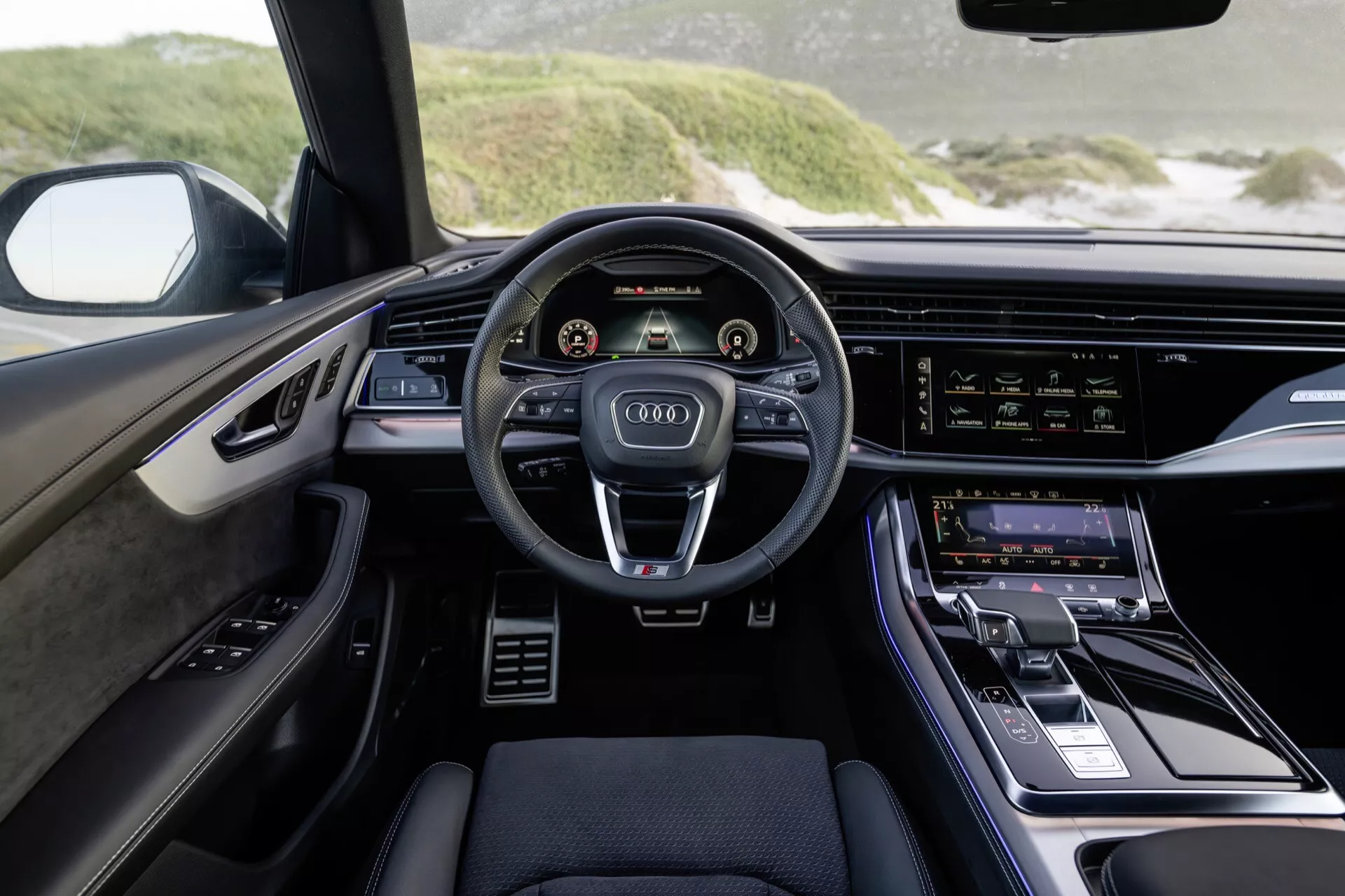 Notranjost Audi Q8 2023 (4M-Facelift) iz perspektive voznika poudarja sodobno armaturno ploščo, volan s tremi kraki z nadzornimi gumbi, dvojni digitalni zasloni za instrumente in sistem za informacije in zabavo ter razkošne oblikovalske poudarke.