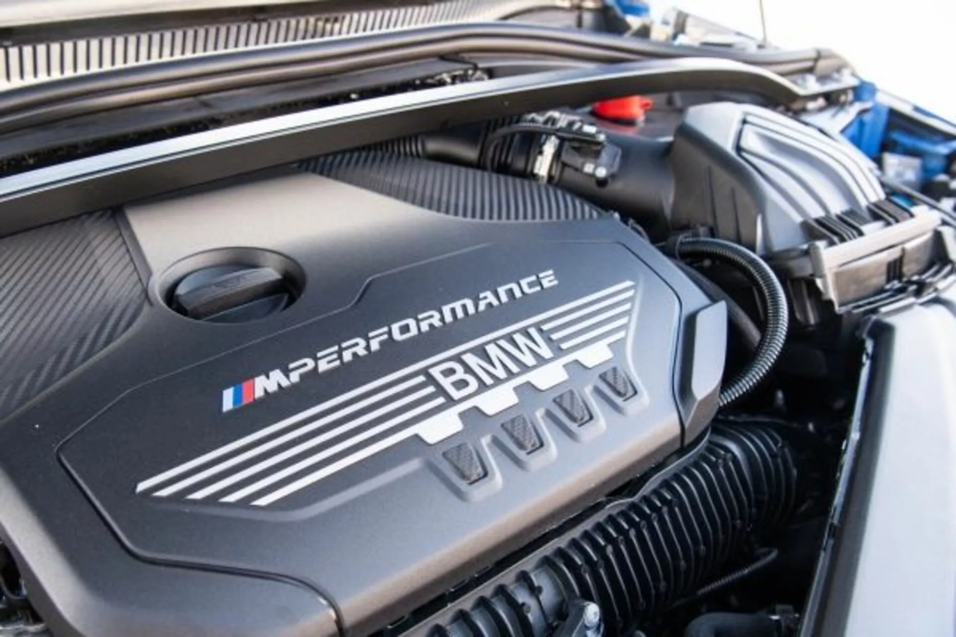 Podroben pogled na pokrov motorja BMW serije 1 M Performance 2019 z logotipom BMW in barvami divizije M v dobro vzdrževanem motorju