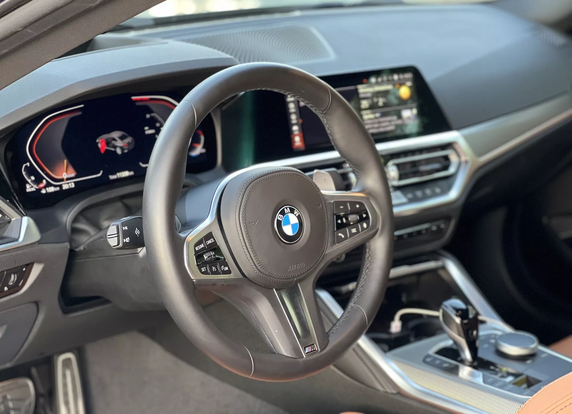Notranji pogled na BMW serije 2 Coupe 2022 s perspektive voznika, s centralno nameščenim volanom z večfunkcijskimi gumbi, digitalnim instrumentom, ki prikazuje hitrost in merilnik vrtljajev, centralni digitalni zaslon z GPS navigacijo in kakovostnimi materiali, vključno z usnjenimi površinami in skrbno oblikovanimi zaključnimi elementi v kabini.