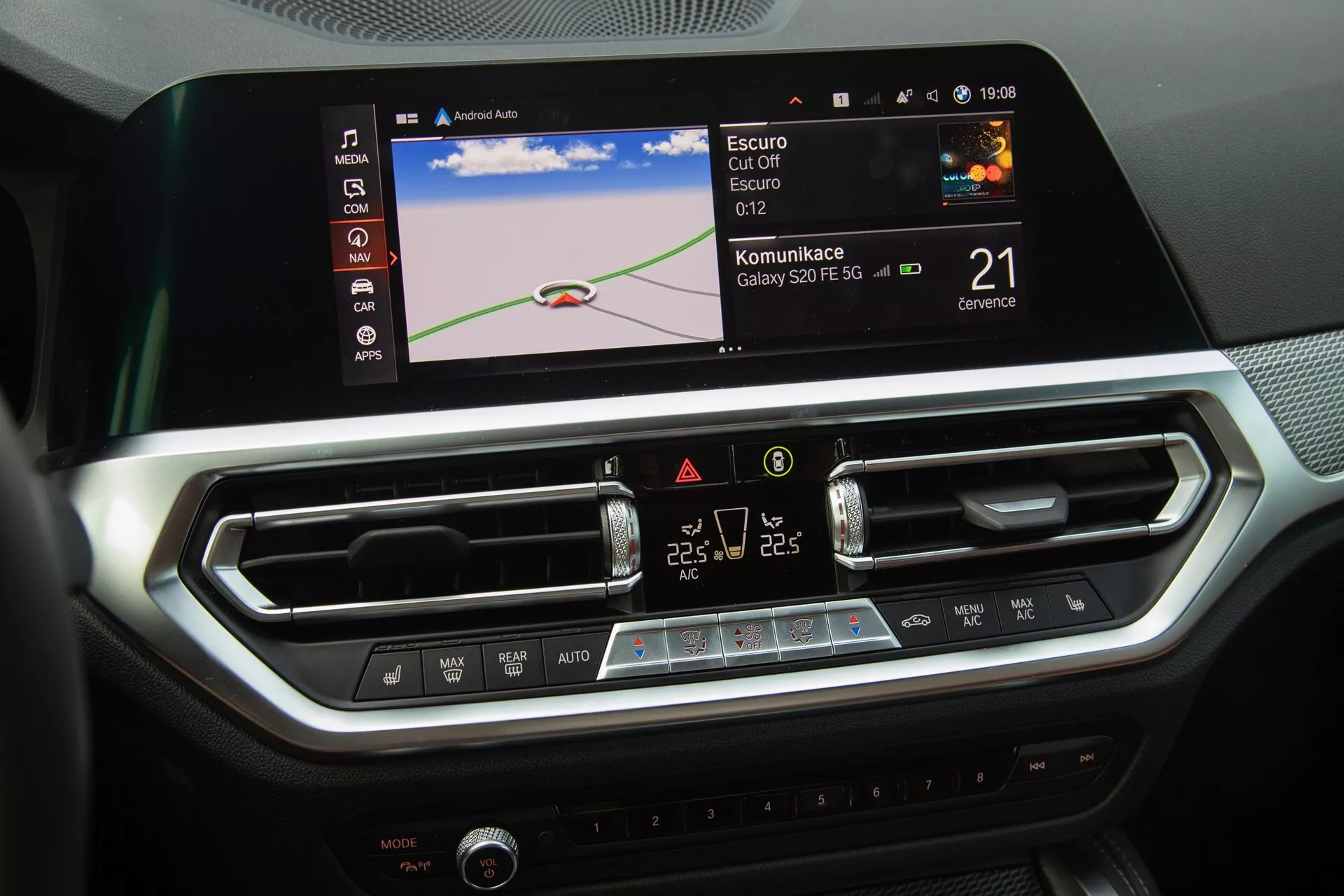 Osrednja konzola BMW 2-Series Coupe 2022 je izpostavljena, kar poudarja sodoben informacijsko-zabavni sistem in nadzore klimatskih naprav avtomobila. Slika prikazuje velik barvni zaslon na dotik z navigacijsko karto, ikonami za integracijo Bluetooth ali pametnih telefonov in uro. Pod zaslonom sta dve osrednji zračni šobi z nastavljivimi loputami in eleganten panel z gumbi na dotik in LCD zaslonom za dvopodročno klimatsko napravo. Notranji dizajn z brušenimi kovinskimi poudarki in teksturami, podobnimi ogljikovim vlaknom, odraža razkošno in tehnološko usmerjeno okolje.