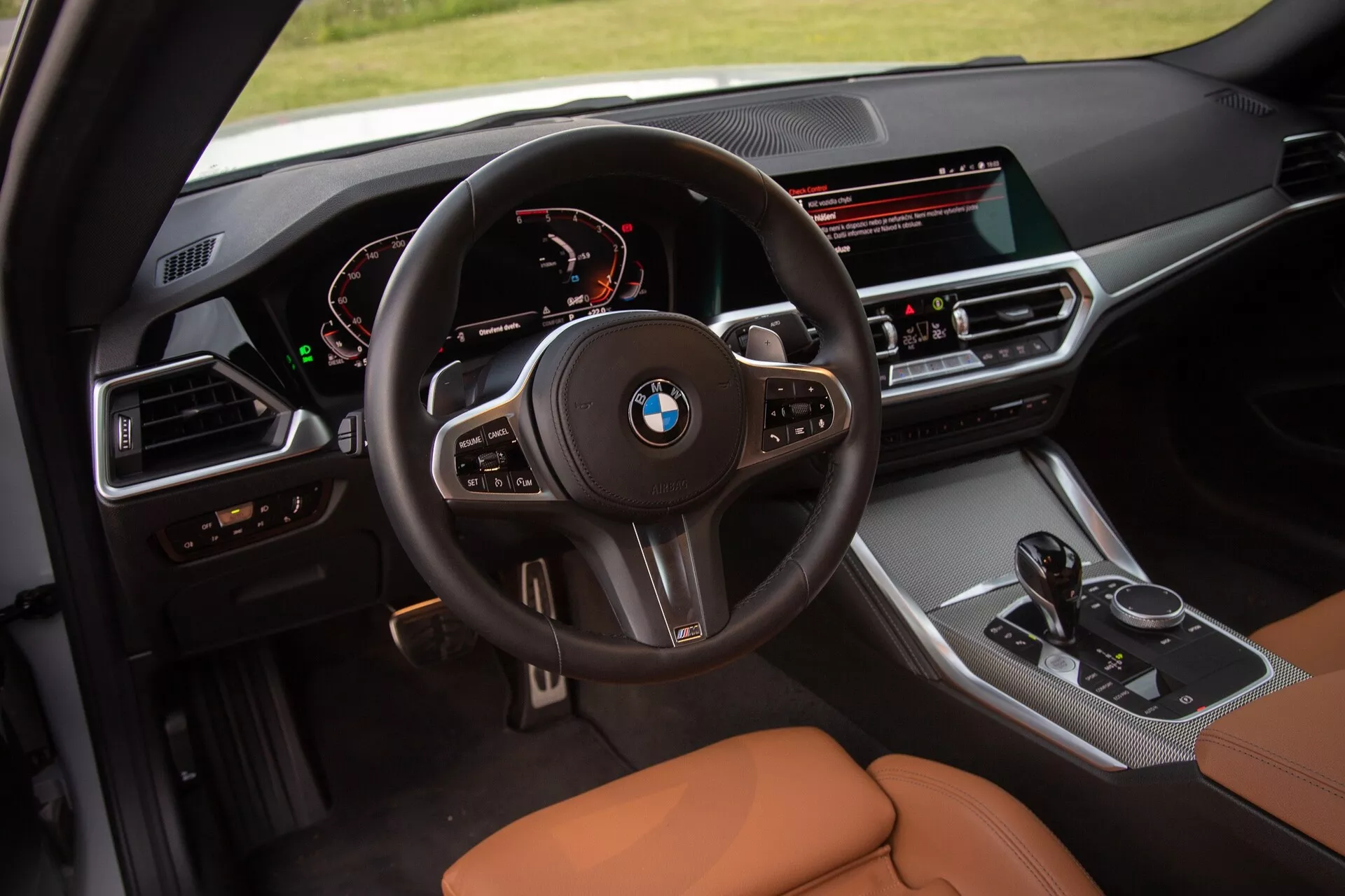 Notranja slika 2022 BMW serije 2 Coupe, usmerjena na kokpit voznika. Dvigajoč zorni kot omogoča podroben pogled na večfunkcijski volan z logotipom BMW, digitalno armaturno ploščo, ki prikazuje merilnik hitrosti in tahometer, ter vozniku usmerjeno sredinsko konzolo s širokim zaslonom infotainment, gumbi za klimatsko napravo, prestavno ročico in izbirnikom iDrive. Sedeži so oblazinjeni s karamelno ali rjavo usnje, kar poudarja razkošje in udobje.