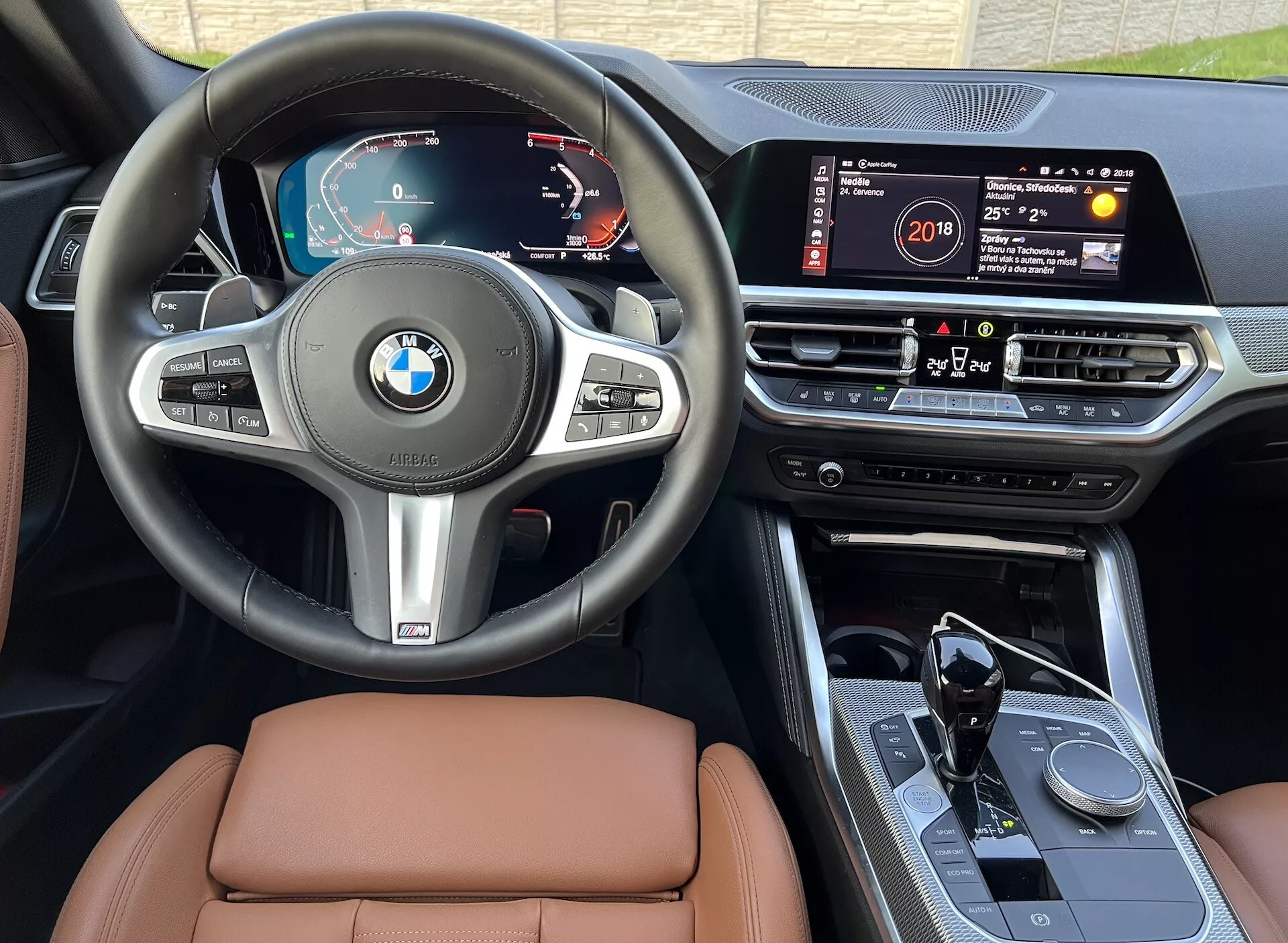 Posnetek notranjosti BMW serije 2 Coupe 2022, ki prikazuje armaturno ploščo, volan in sredinsko konzolo. Značilnosti vključujejo digitalno instrumentno ploščo, večfunkcijski volan, velik zaslon na dotik z informacijskim sistemom, vrtljiv kontrolni gumb na sredinski konzoli, avtomatsko prestavno ročico s športno zasnovo in visokokakovostne usnjene sedeže, vse iz perspektive voznikovega sedeža pri naravni dnevni svetlobi.