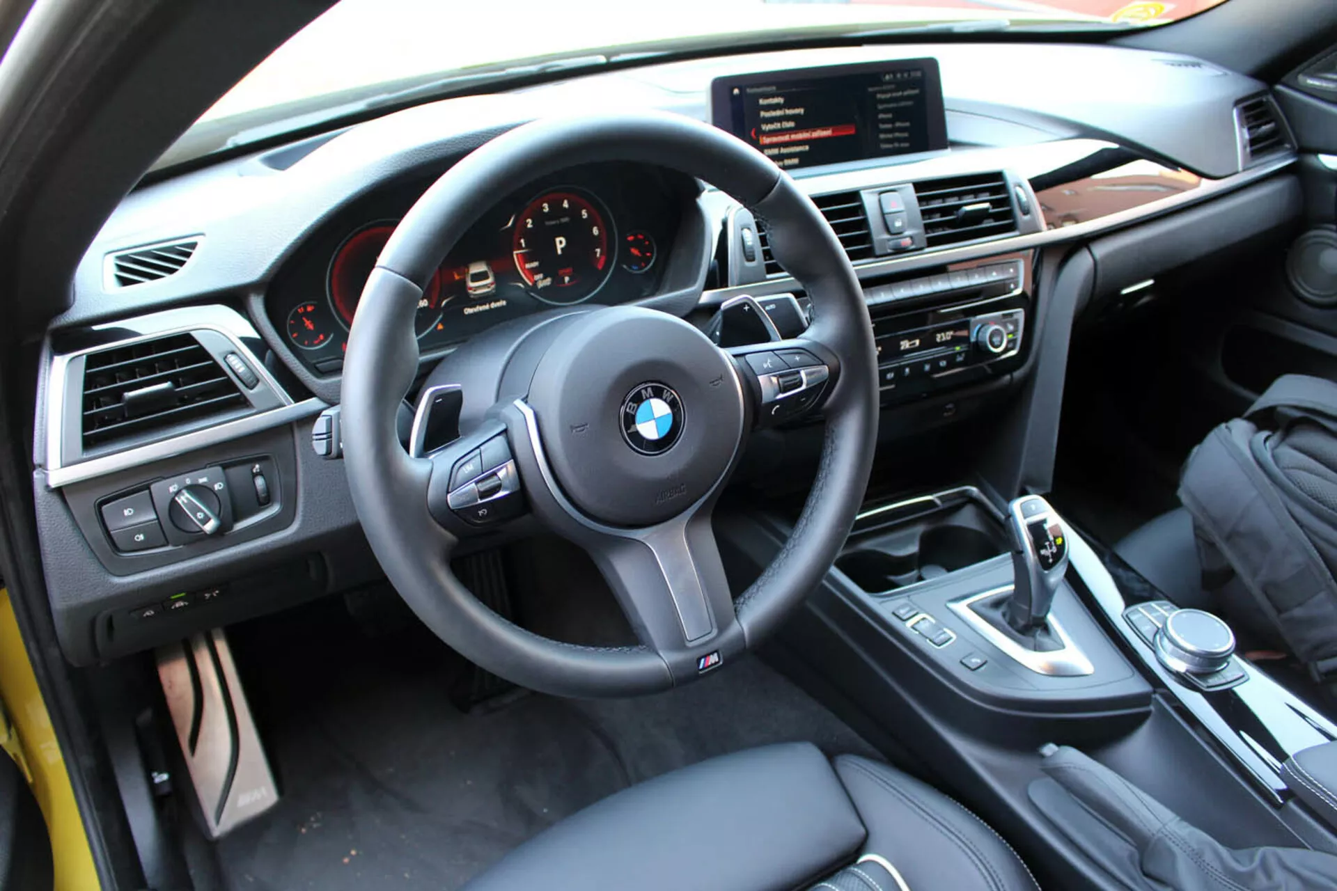 Notranji pogled na BMW serije 4 Coupe iz leta 2013 iz perspektive voznika, ki prikazuje volan, armaturno ploščo, sredinsko konzolo z multimedijskimi in klimatskimi kontrolami, prestavno ročico in luksuzne finiše