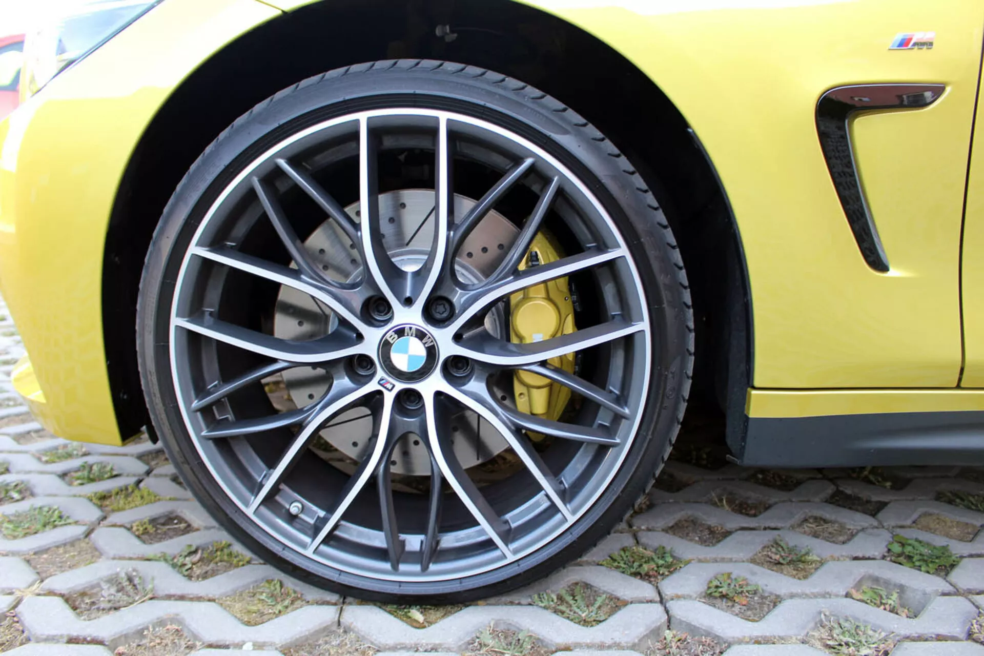 Pogled od blizu na sprednje kolo BMW serije 4 Coupé 2013 s temno sivim večkrakim dizajnom iz zlitine, nizko profilno radialno brez zračno pnevmatiko, z visoko zmogljivim zavornim sistemom s prečno vrtanimi zavorami in rumenimi zavornimi čeljustmi, ob svetlo rumenem športnem telesu
