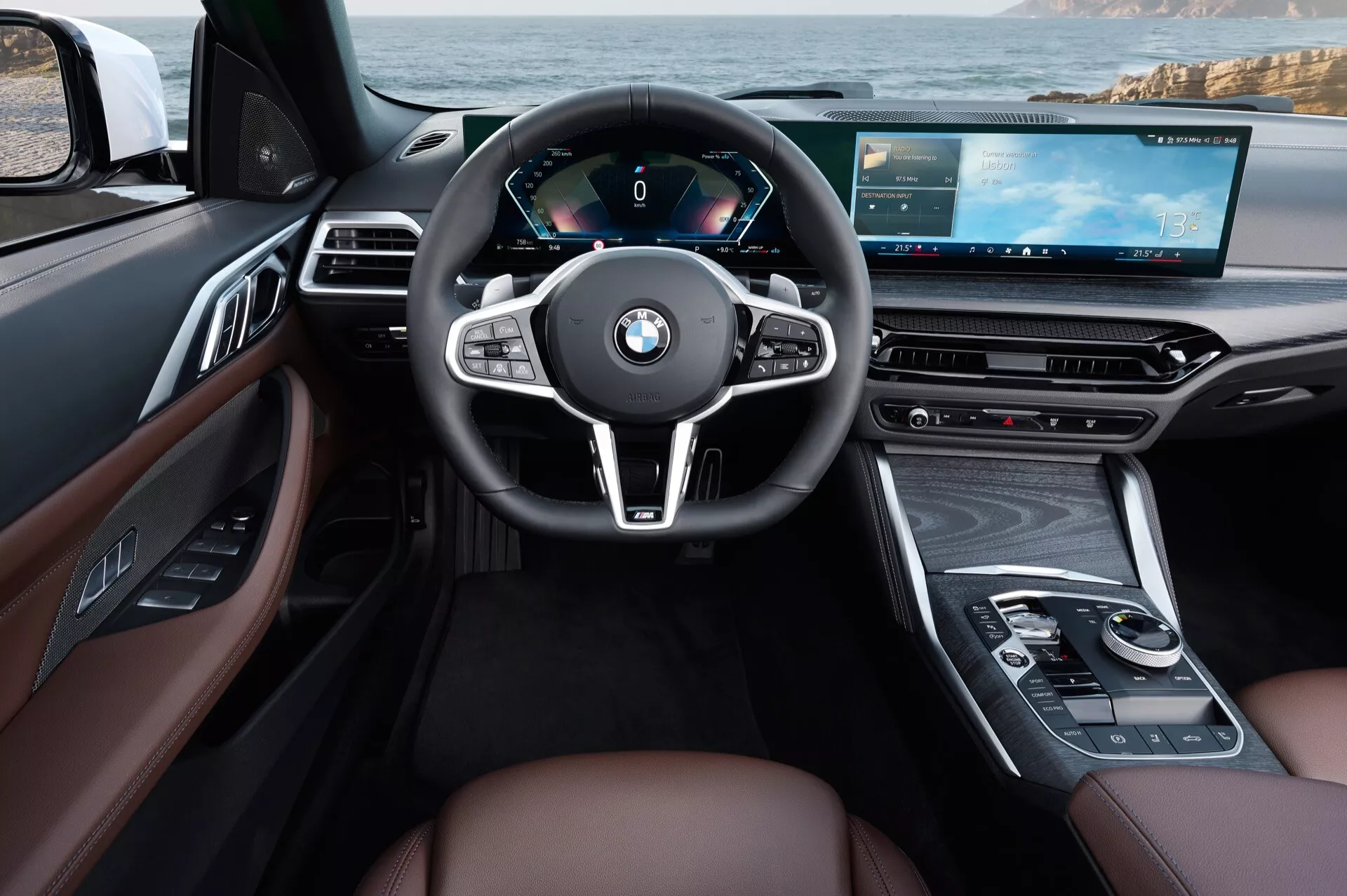 Notranji pogled na BMW serije 4 2024 (G22-G23-G26-G82-G83-facelift) iz perspektive voznika z volanom, ovitim v usnje, s tremi kraki, popolnoma digitalnim instrumentnim sklopom, napredno multimedijsko sredinsko konzolo z zaslonom na dotik, razkošnimi usnjenimi sedeži v rjavi barvi z lesnimi poudarki in modernimi ergonomskimi lastnostmi, vključno z multifunkcijskimi kontrolami in digitalno armaturno ploščo