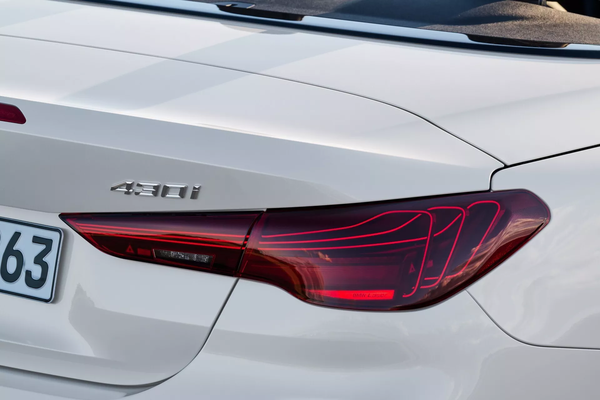 Podroben pogled na zadnji kot BMW serije 4 letnik 2024 (G22-G23-G26-G82-G83-Facelift) z LED zadnjo lučjo, hibridno značko '450h' in delom prtljažnika v srebrno-beli barvi
