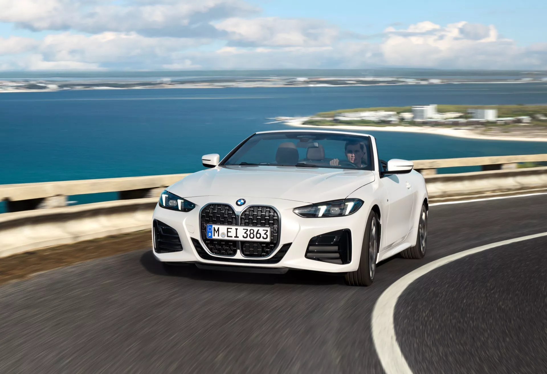 BMW Serija 4 Kabriolet 2024 (preoblikovanje G22-G23-G26-G82-G83) v gibanju na obalni cesti s spuščeno streho, LED žarometi, dvojno ledvičko rešetko in športnimi liti platišči