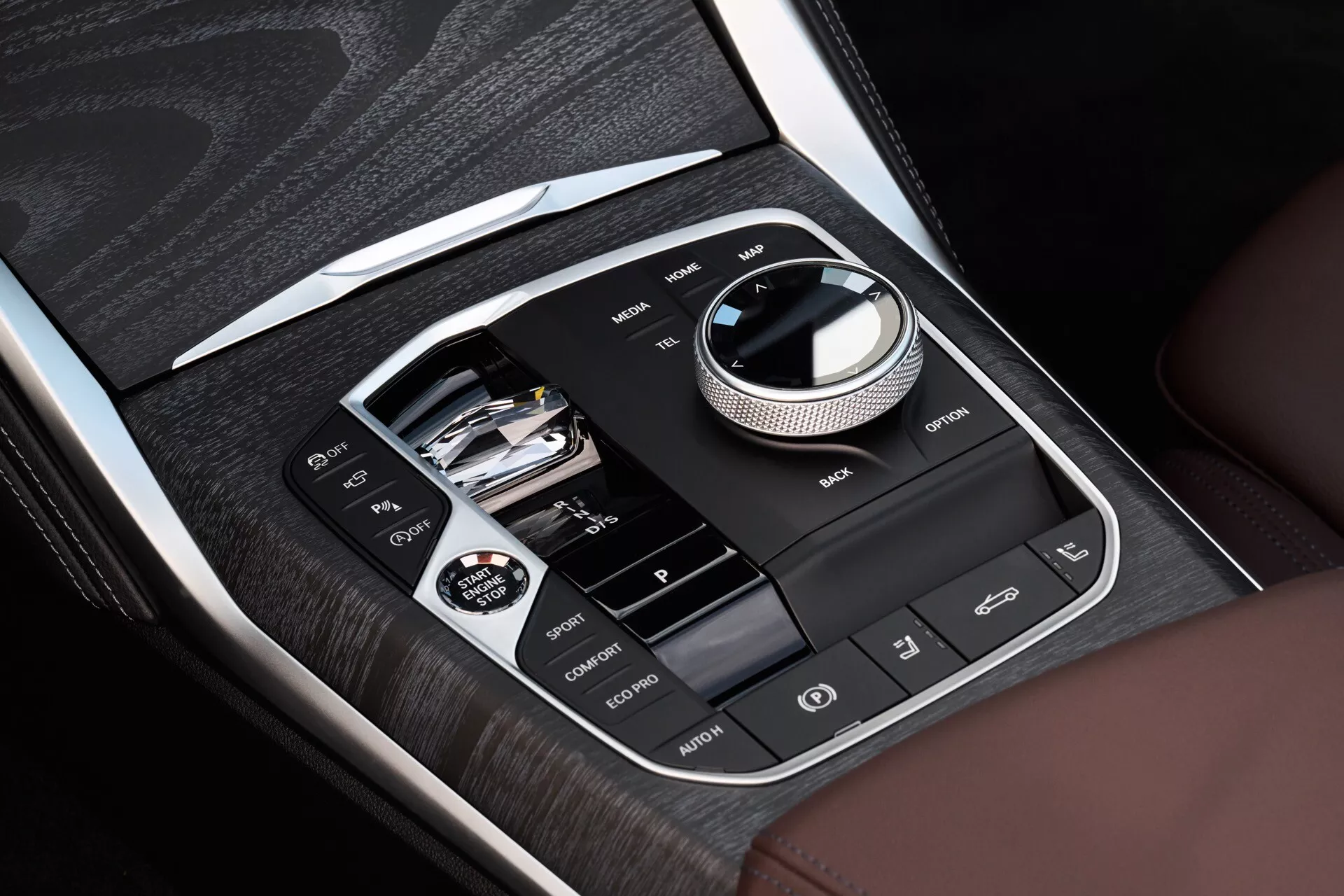 Pogled od blizu na osrednjo konzolo v BMW serije 4 iz leta 2024 (preoblikovanje G22-G23-G26-G82-G83) prikazuje informacijske in nadzorne sisteme z lesno furnirjo in kromiranimi poudarki, vključno z glavnim krožnim vmesnikom, povezljivostjo USB in režo za SD kartico, ter gumbi za pomoč vozniku, kot so ogrevanje sedežev in izklop elektronske stabilnosti ESC