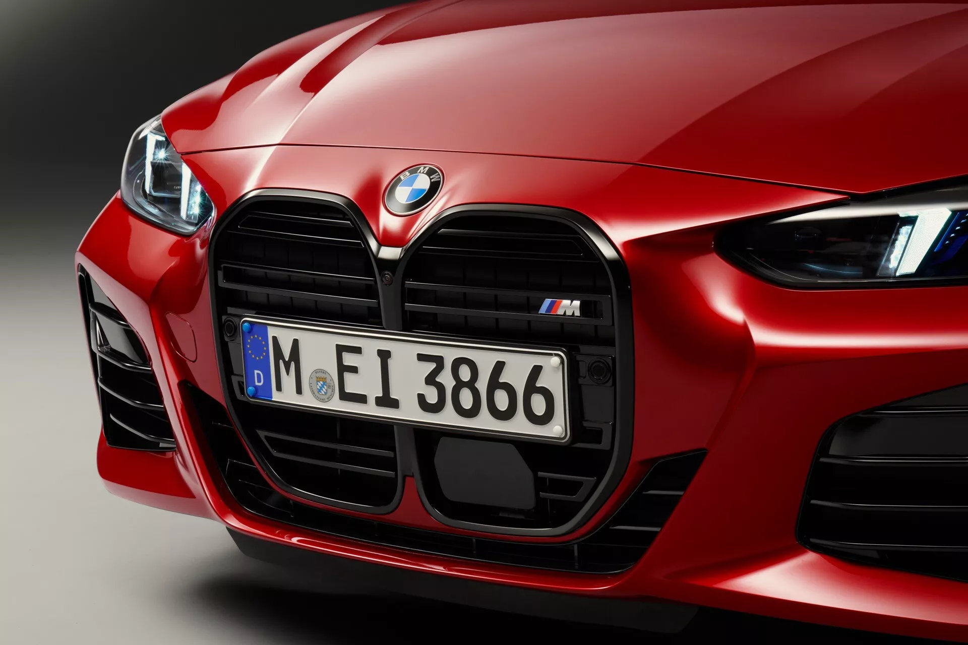 Podroben posnetek sprednjega dela rdečega BMW serije 4 letnik 2024 (G22-G23-G26-G82-G83 Facelift), ki poudarja aerodinamično oblikovanje, izstopajočo ledvično masko serije M s kromiranimi detajli, zmogljive velike zračne vhode in napredne LED žaromete