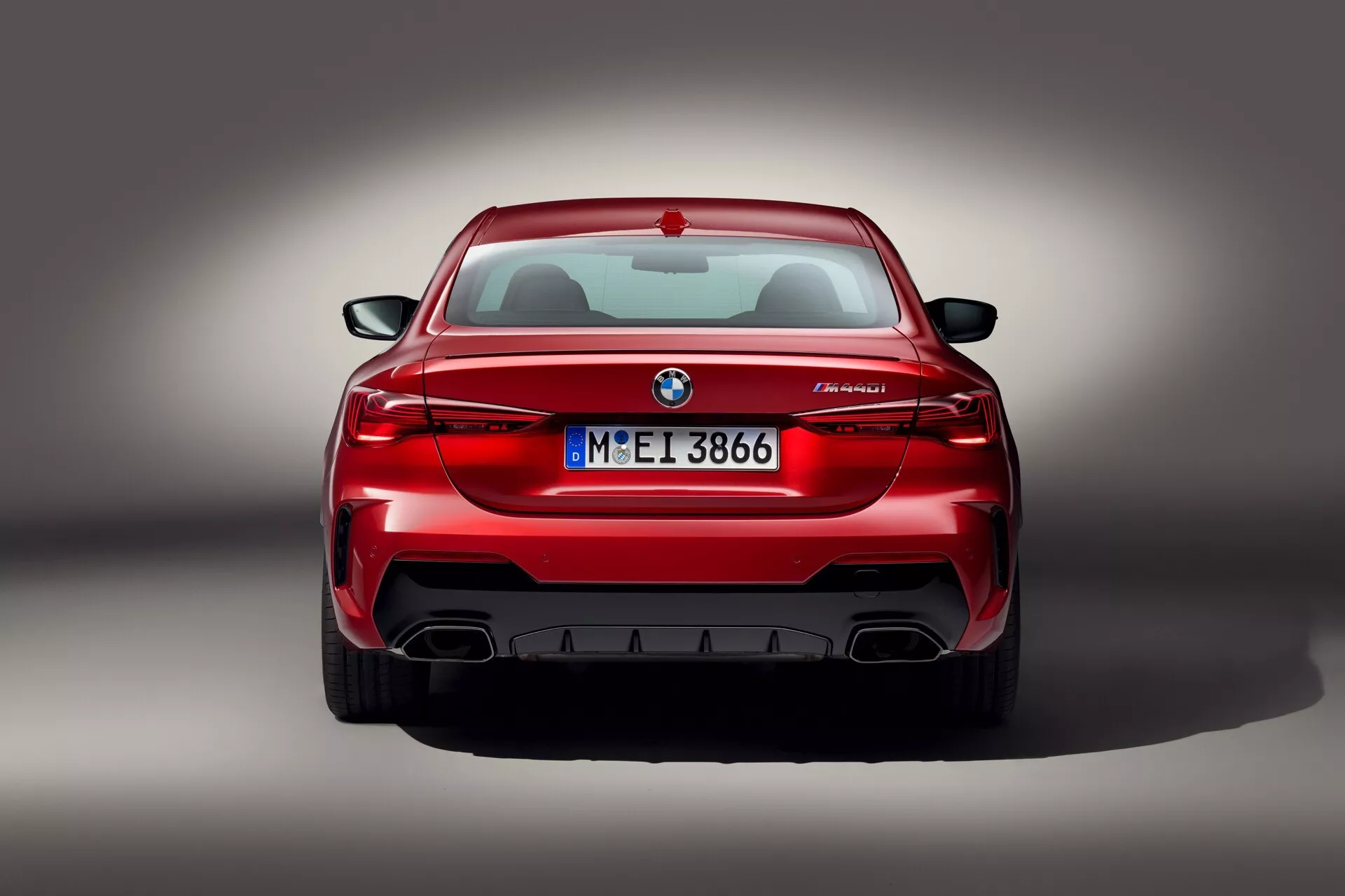 Zadnji pogled na rdeče BMW M5, ki prikazuje L-oblikovane zadnje luči, emblem, oznako modela M5 in dvojne izpušne cevi z difuzorjem, studijski posnetek s profesionalno razsvetljavo