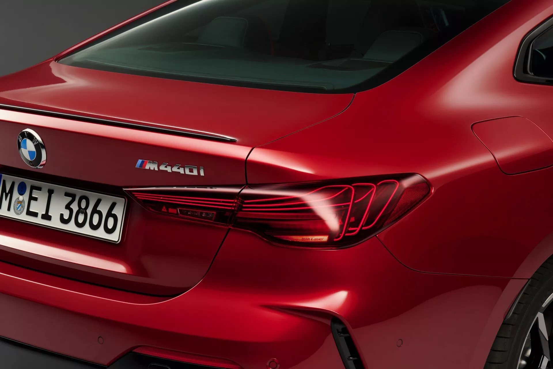 Podroben pogled na zadnjo četrtino rdečega BMW M440i 2024, vključno z elegantno vodoravno zasnovo zadnje luči, oblikovanim zadnjim blatnikom in oznako M Performance na pokrovu prtljažnika.