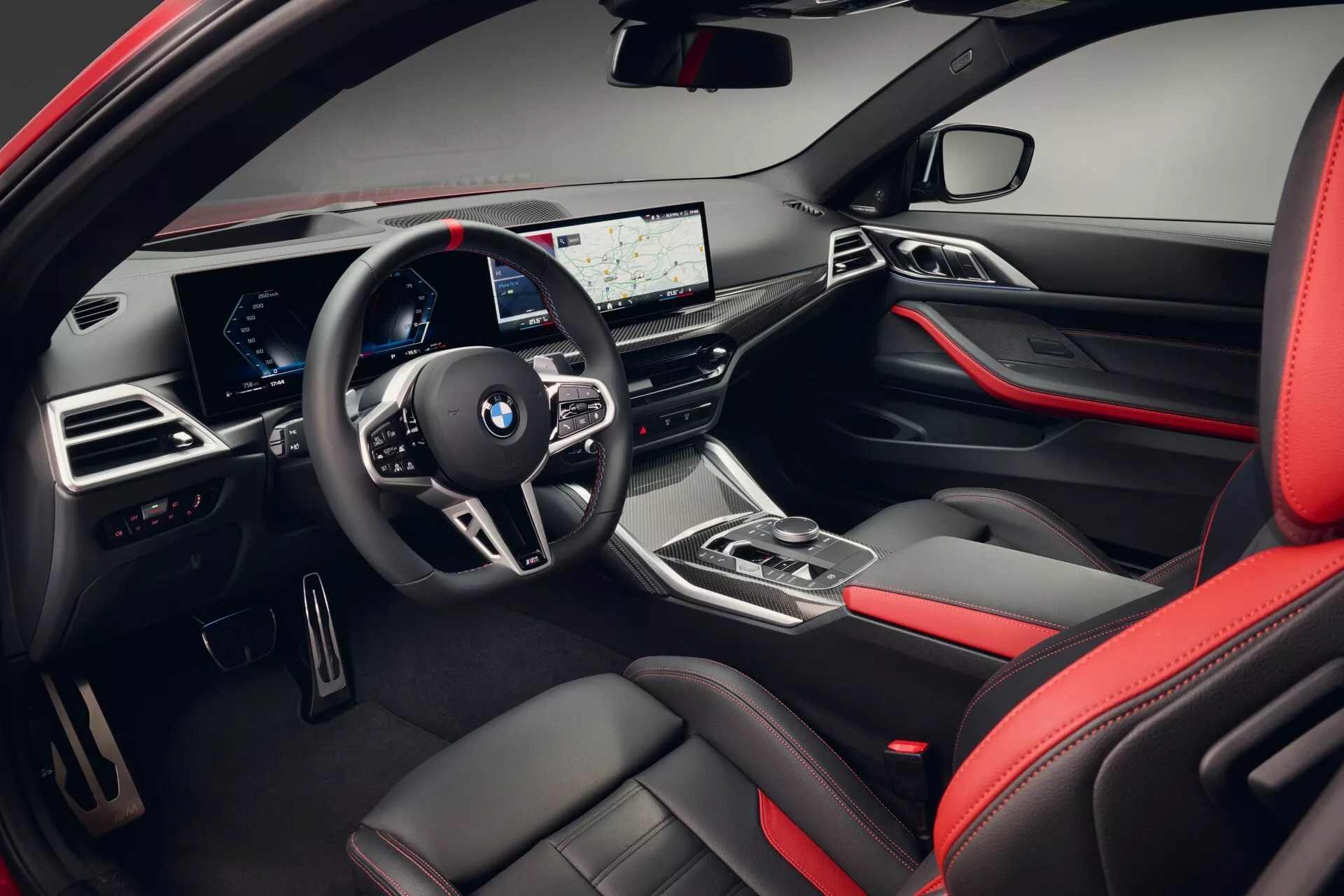 Pogled na notranjost BMW serije 4 2024 (G22 G23 G26 G82 G83 Facelift) prikazuje stranico voznika, vključno z armaturno ploščo in območjem volana z multimedijskimi kontrolami, digitalnim instrumentnim sklopom, širokozaslonskim zaslonom za informacije in zabavo, ergonomsko ročico menjalnika, visokokakovostnimi materiali z rdečimi poudarki in naprednimi tehnološkimi značilnostmi.