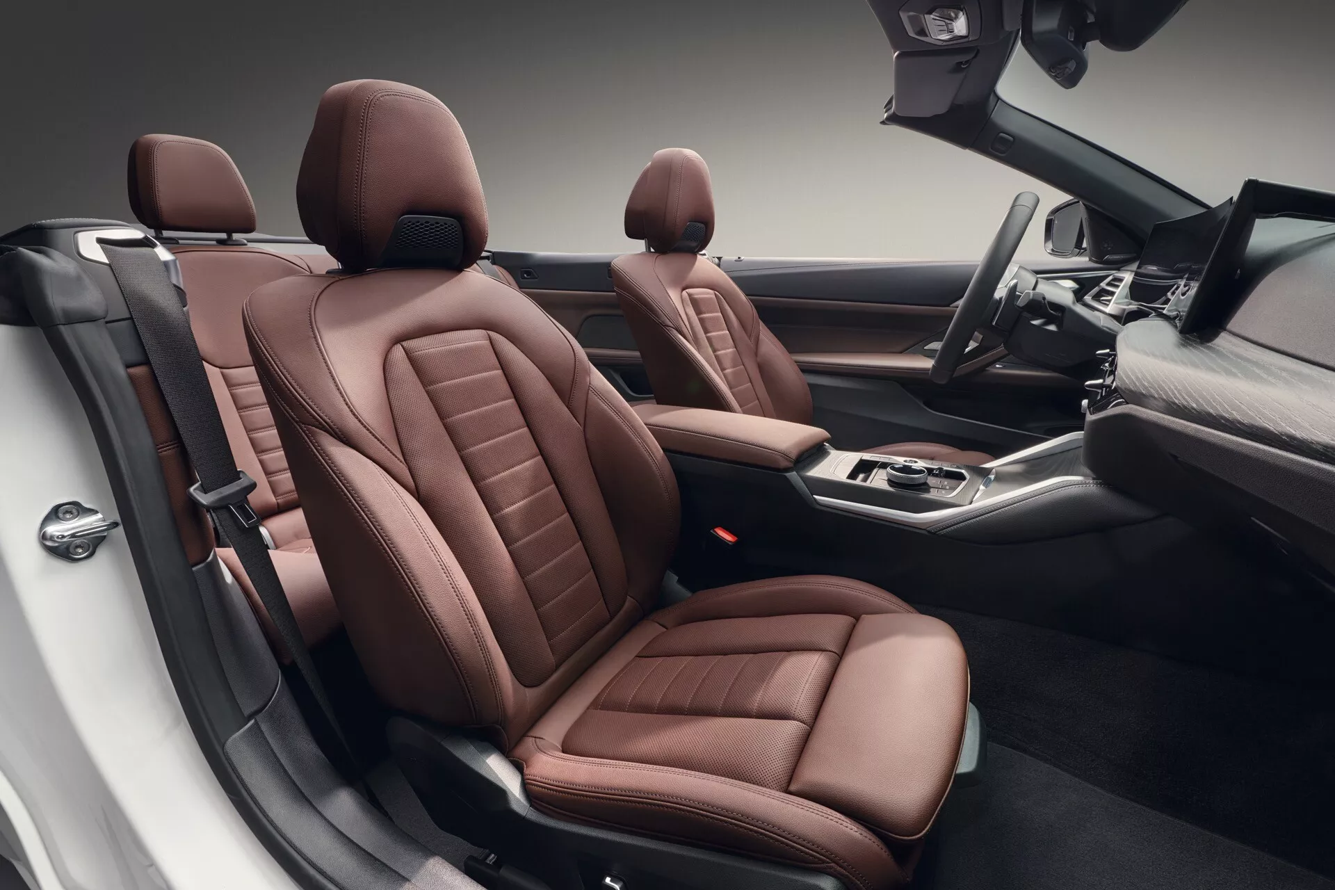 Notranji pogled na BMW serije 4 letnik 2024 (G22-G23-G26-G82-G83 facelift) z zgornje perspektive prikazuje razkošne rjave usnjene sedeže z zapletenim šivanjem, napredne kontrole na sredinski konzoli in prostorno zasnovo kabine, ki poudarja sofisticirano obrtništvo in sodobne tehnološke ugodnosti.