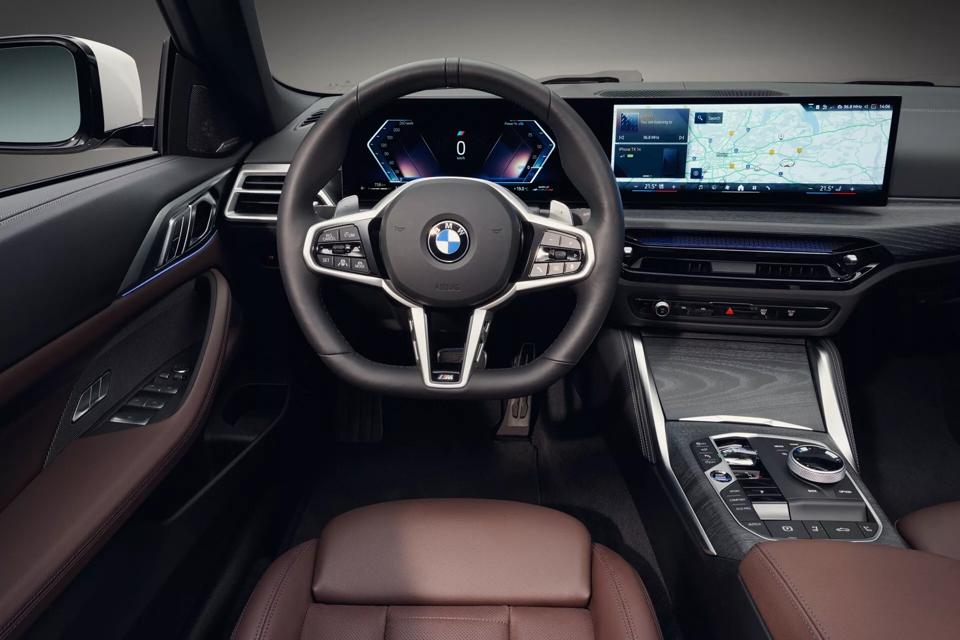 Notranjost BMW serije 4 2024 (G22-G23-G26-G82-G83 Facelift), osredotočena na voznikov prostor z digitalno armaturno ploščo, multifunkcijskim volanom, velikim zaslonom za informacijsko-zabavni sistem z navigacijo, razkošnimi zaključki iz usnja in lesa, iz perspektive prve osebe