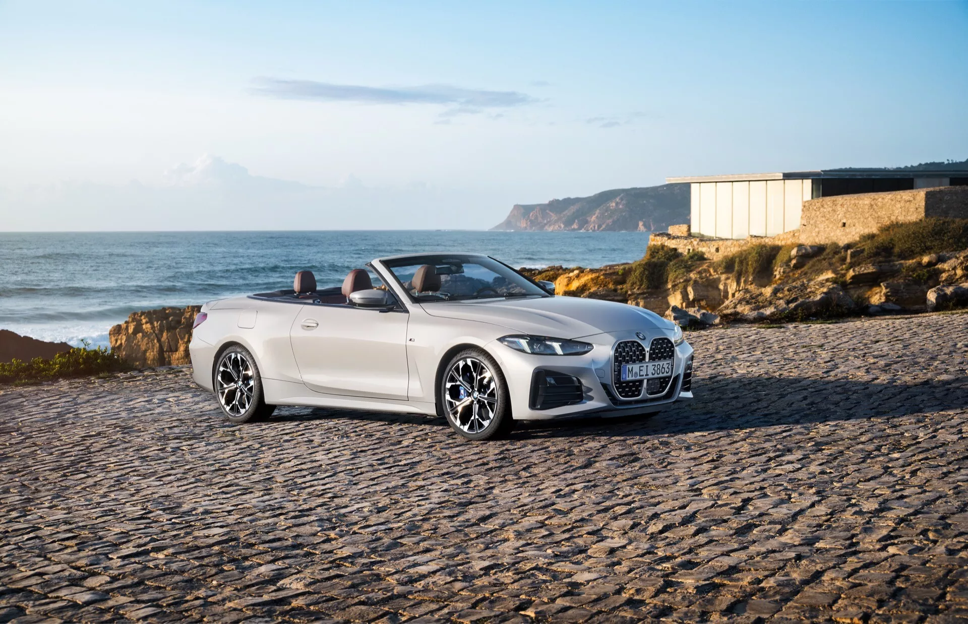 BMW serije 4 kabriolet (G22-G23-G26-G82-G83 prenova) letnik 2024, parkiran na obaljenem območju v obalnem okolju, prikazuje sprednji levi strani, LED žaromete, veliko masko z mrežo in elegantna lita kolesa pod toplim svetlom poznega popoldneva