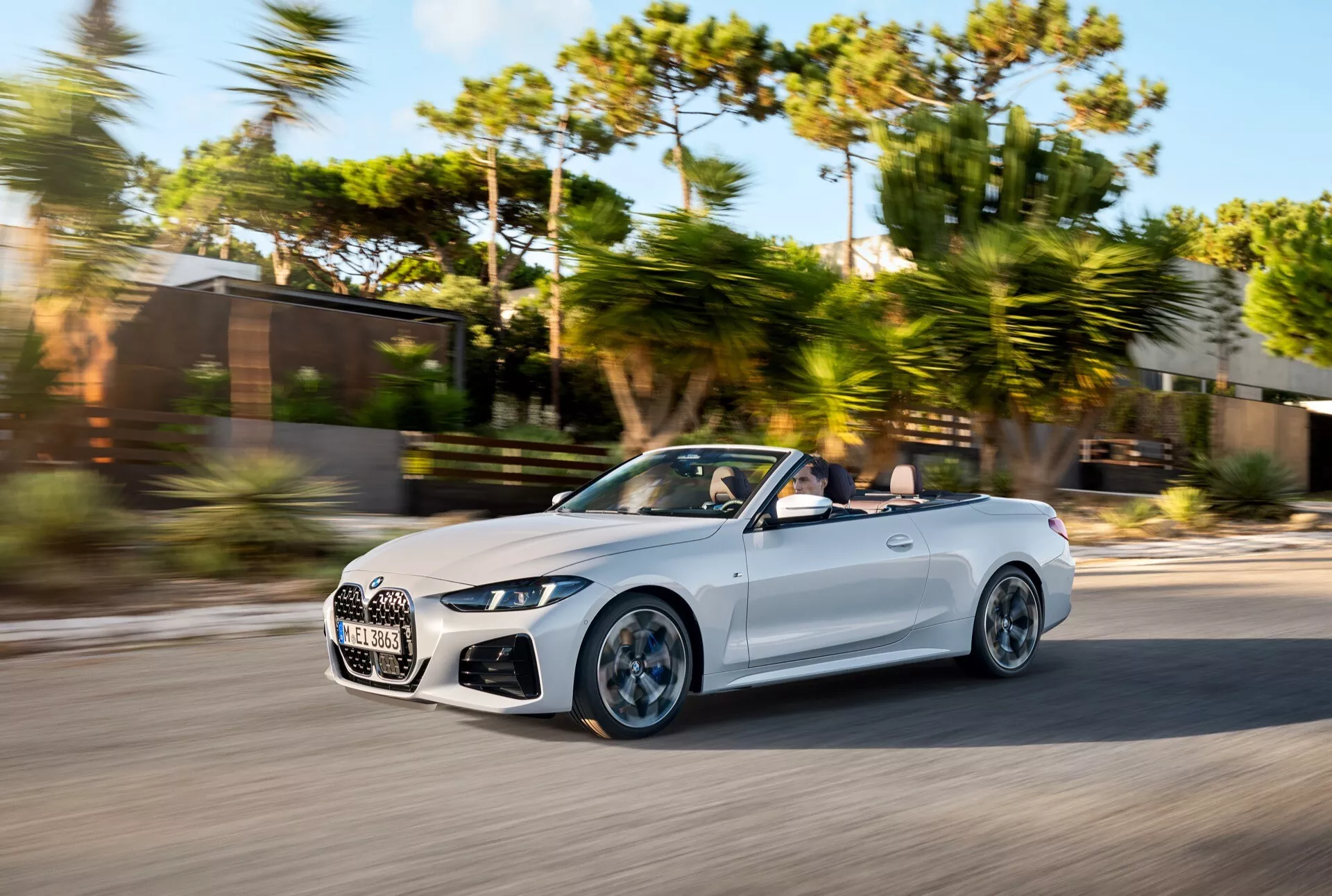 Kabriolet BMW serije 4 2024 (preoblikovanje G22-G23-G26-G82-G83) v gibanju, posnet z zornega kota tri četrtine spredaj z poudarkom na aerodinamiki, premijski rešetki in LED žarometih na sončen dan z zamegljenim ozadjem.