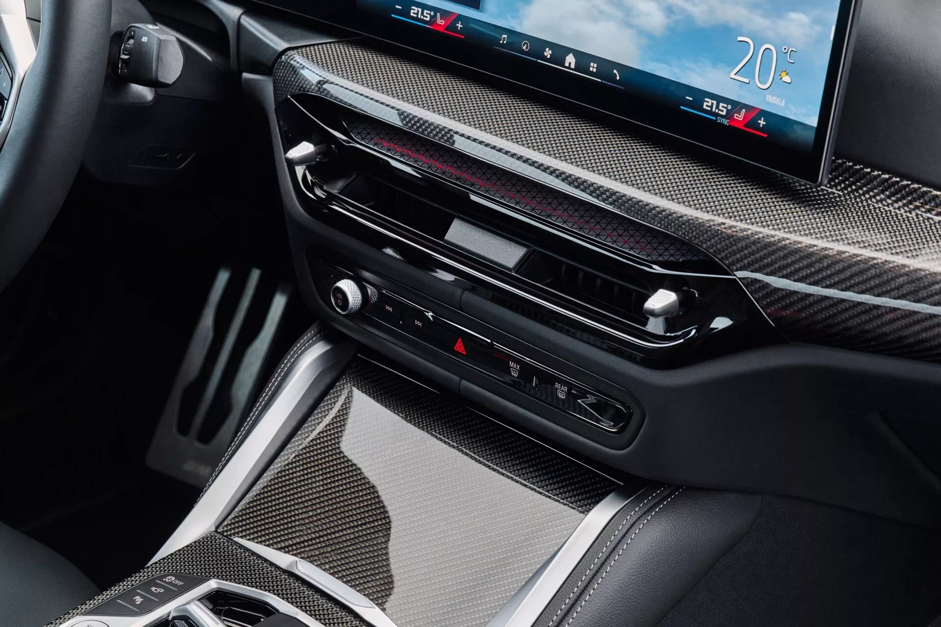 Podroben notranji pogled na BMW serije 4 modela 2024, ki prikazuje področje sredinske konzole s trimom iz ogljikovih vlaken, velik digitalni zaslon za infotainment in nadzor klime, tanke zračnike, taktilne gumbe, vključno z nadzorom opozorilnih luči, in sodobno elektronsko prestavno ročico, ki simbolizira napredno tehnologijo prenosa in luksuz.