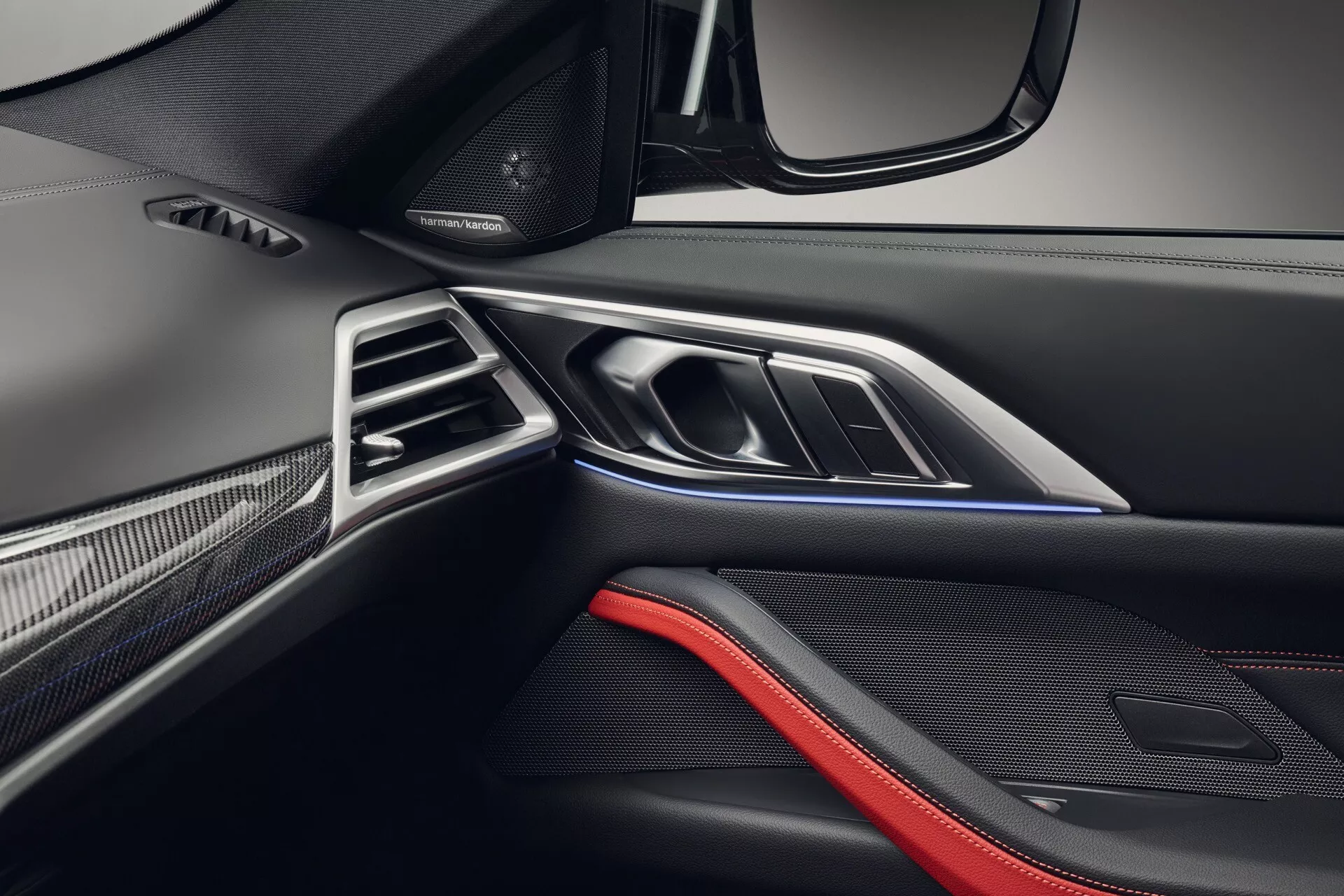 Podroben pogled notranjosti BMW serije 4 2024, ki prikazuje vrata sovoznikove strani in armaturno ploščo s premijskimi materiali in ambientalno osvetlitvijo