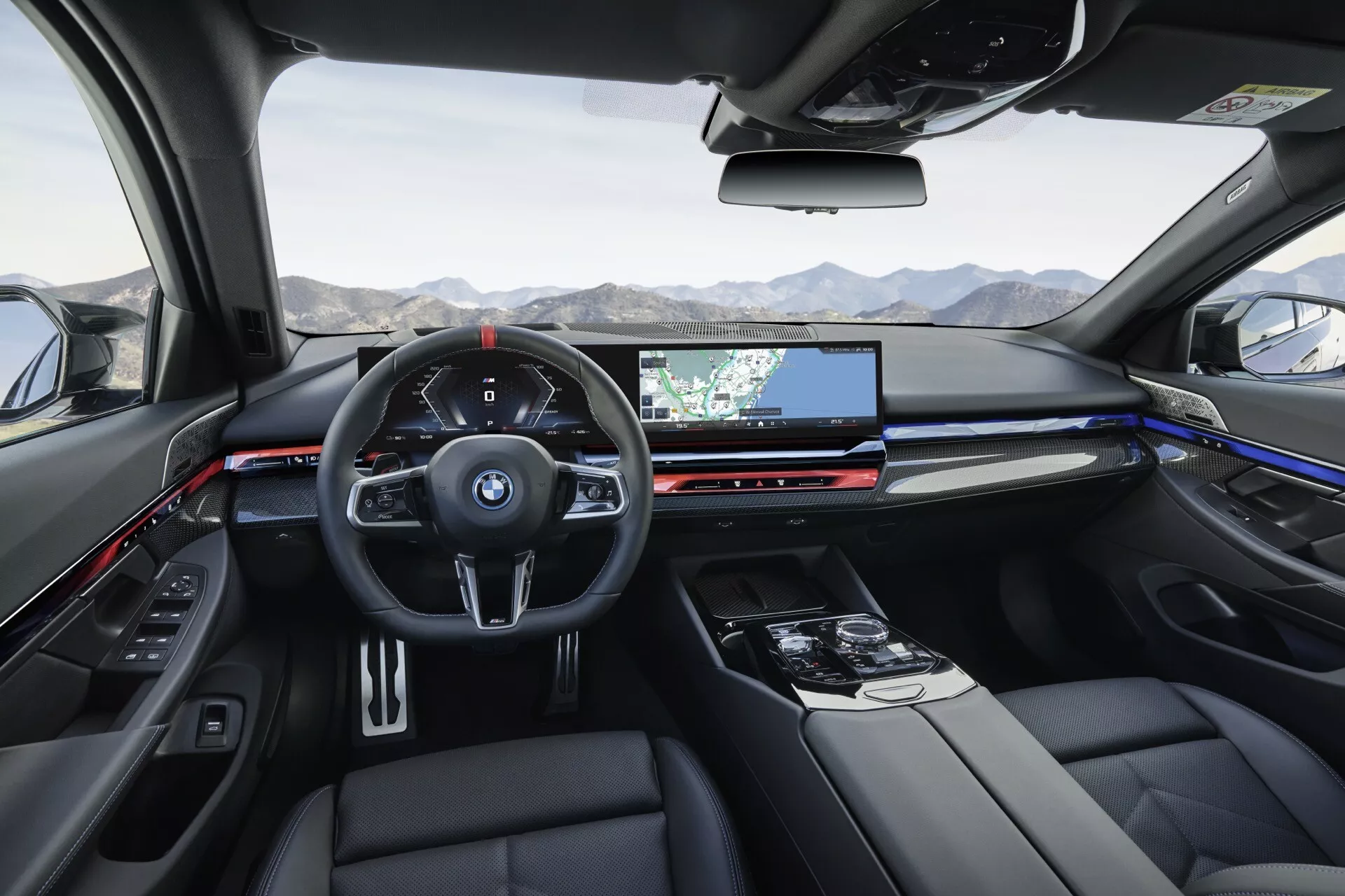 Notranji pogled BMW serije 5 (G60-G61) 2023 s zadnjih sedežev proti digitalni armaturni plošči in širokozaslonskemu infotainment zaslonu z navigacijo, klimatskimi kontrolami, luksuznim oblazinjenjem in panoramsko streho
