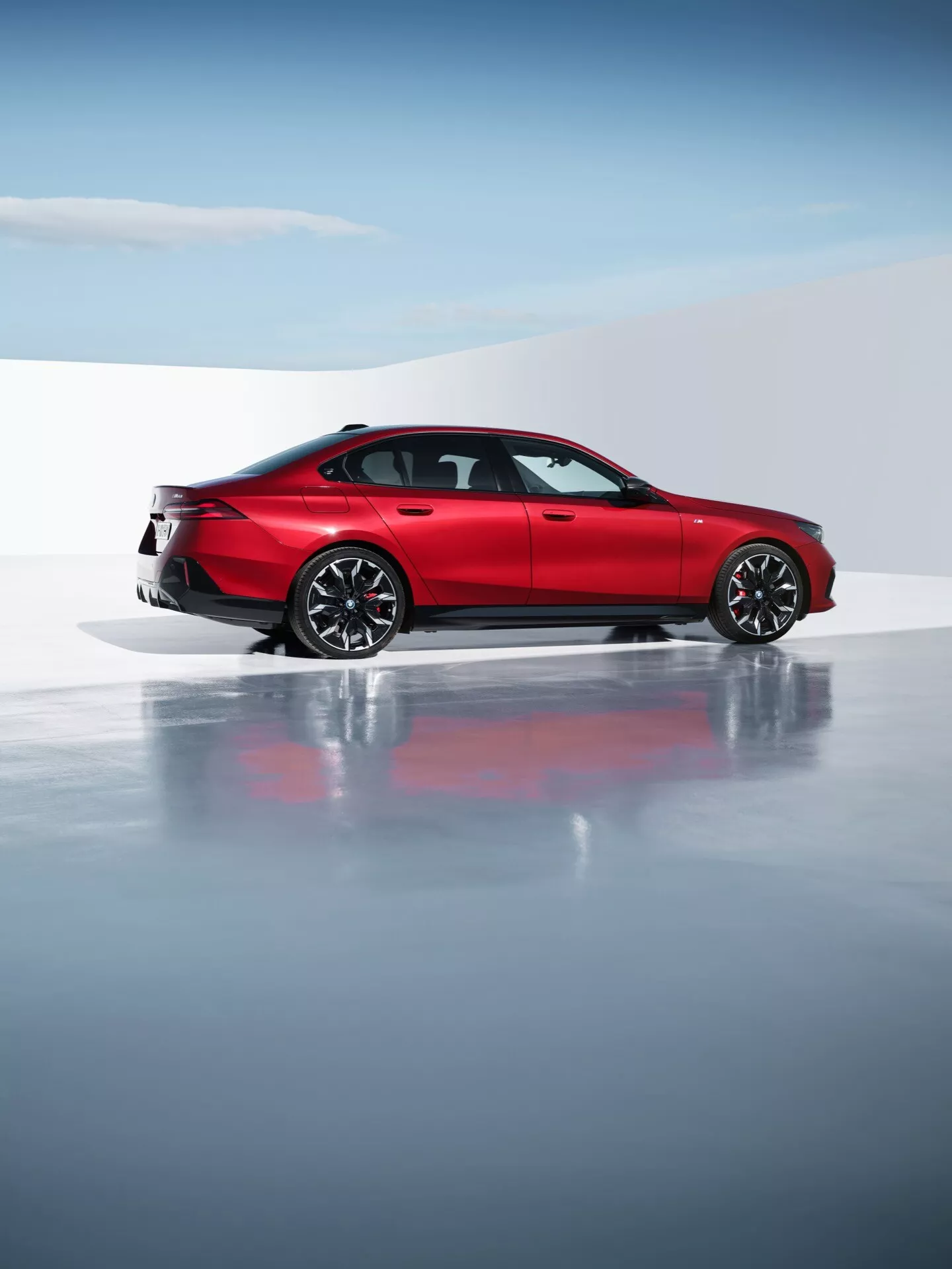 BMW serije 5 (G60-G61) 2023 v živahni rdeči barvi, ki predstavlja svoj aerodinamični dizajn in športno eleganco, z večkrakimi zlitinskimi kolesi, sodobnimi LED zadnjimi lučmi in dvojnim izpušnim sistemom v profesionalni studijski nastavitvi