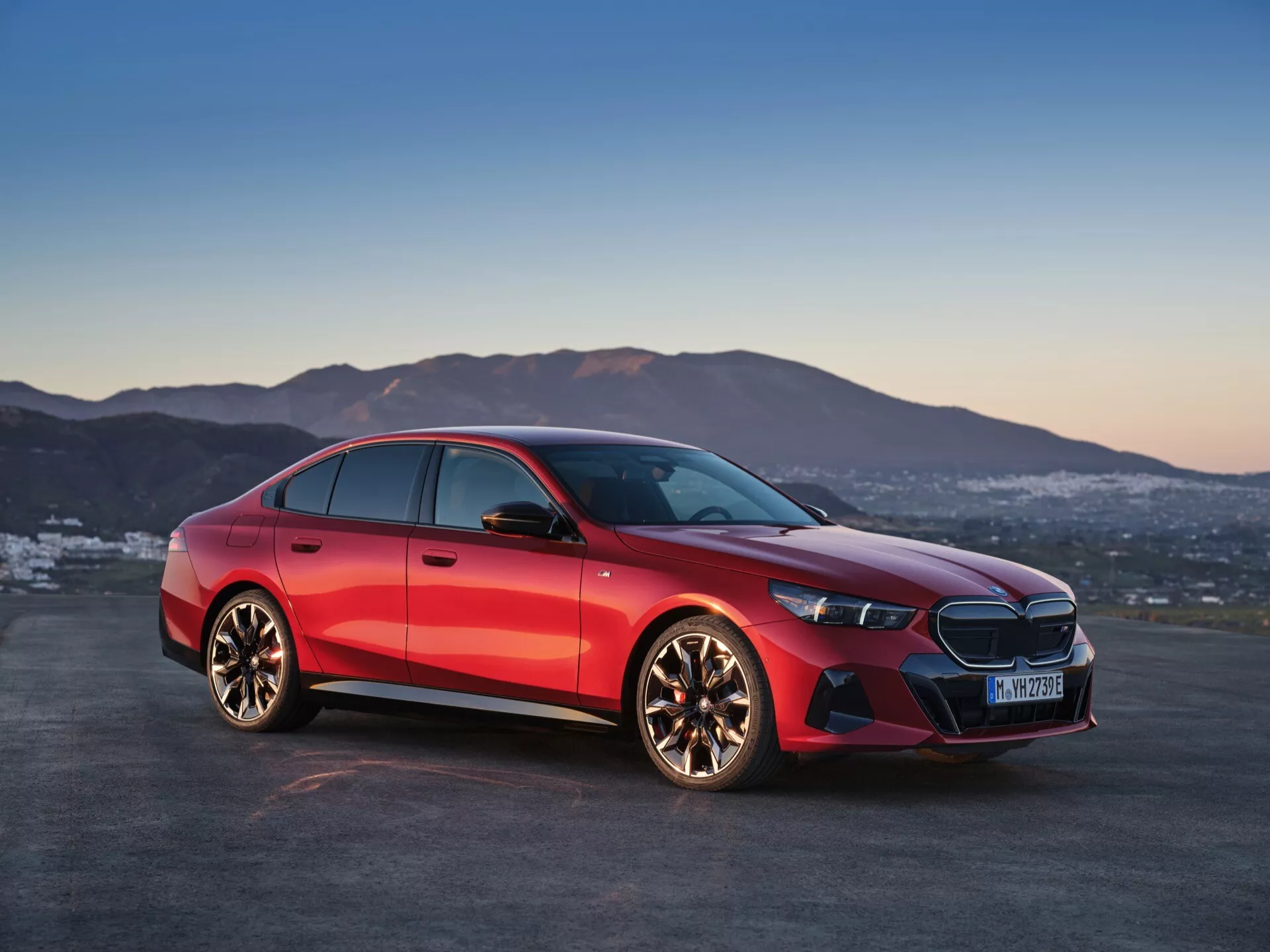 BMW serije 5 iz leta 2023 (G60-G61) prikazan pod kotom tri četrtine spredaj, ki poudarja njegov značilni sprednji žar s središčnim logotipom, elegantne LED žaromete, sprednji odbijač z integriranimi zračnimi vstopi in polirana lita kolesa z večkrakim dizajnom proti dinamični rdeči kovinski zaključni obdelavi in ozadju mraka