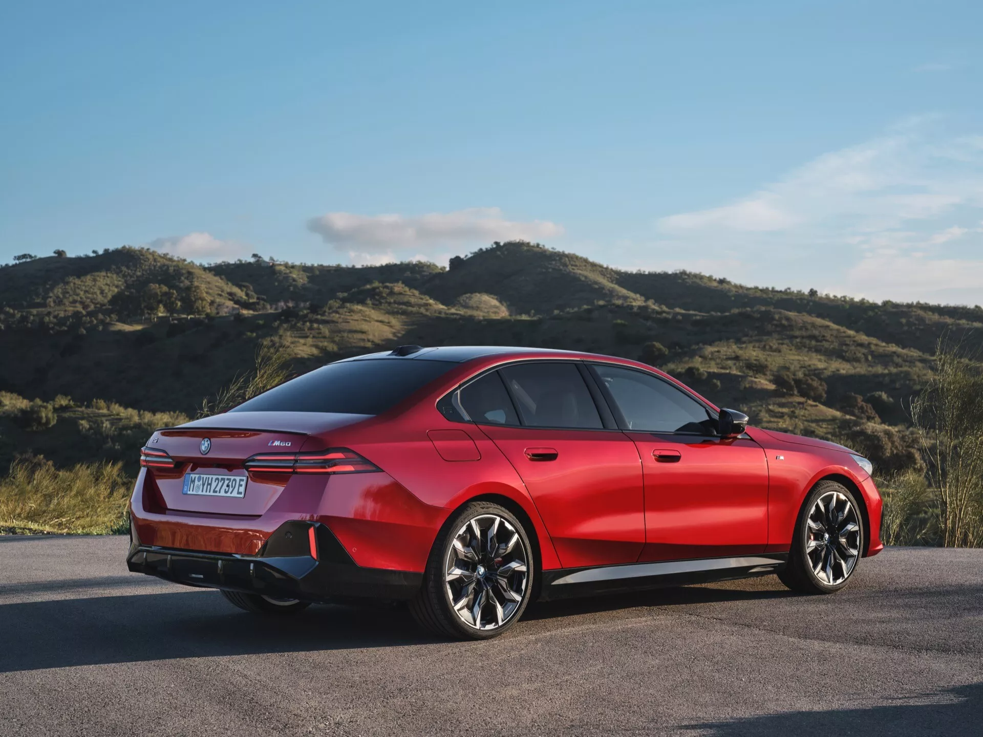 Rdeča štirivratna limuzina BMW serije 5 (G60-G61) letnik 2023, parkirana na prostem, prikazuje svoj zadnji tričetrtinski profil, ki poudarja športno držo vozila, moderno LED podpis zadnjih luči, večkraka lita kolesa in silhueto podobno kupeju.