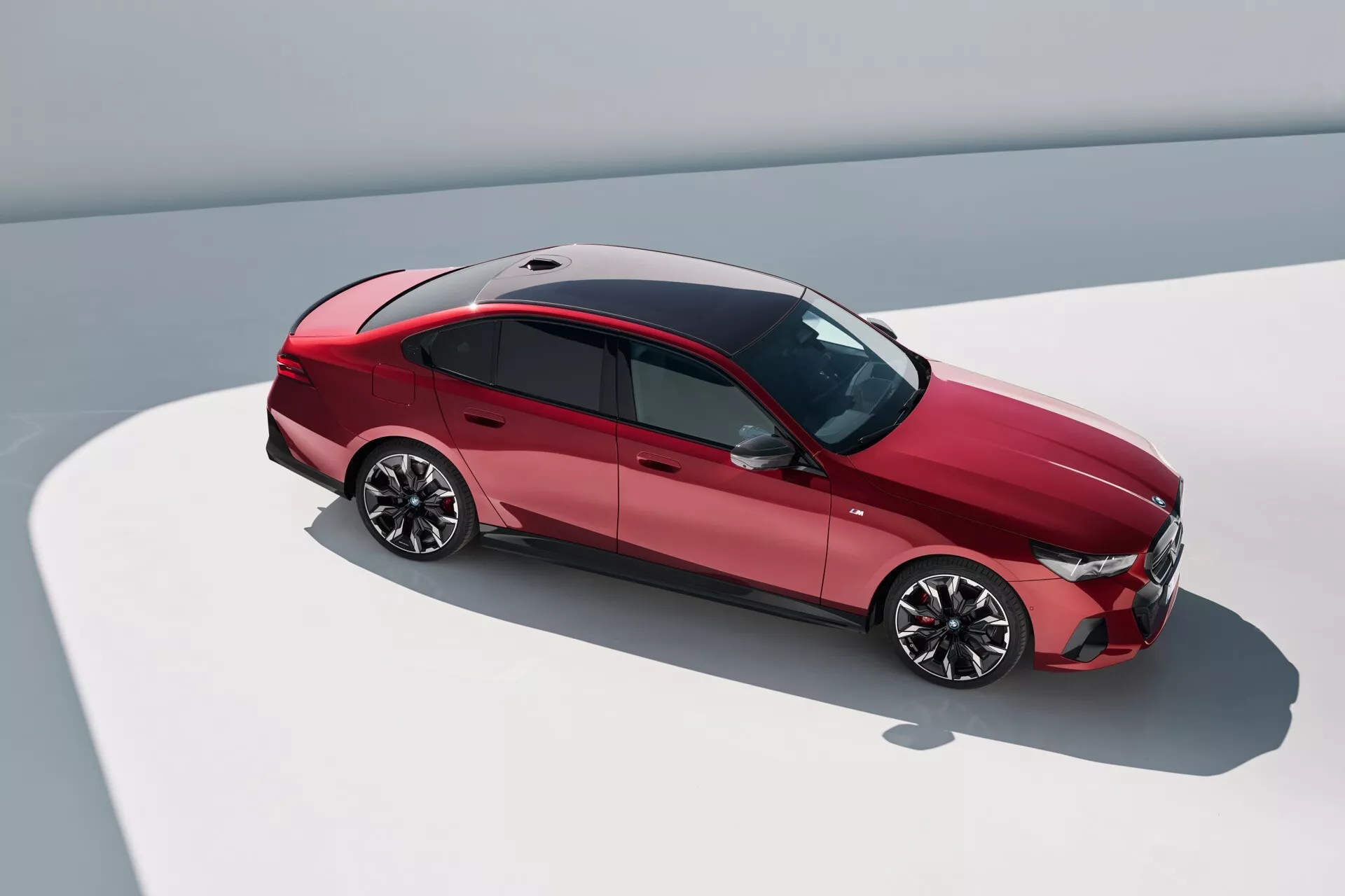 Pogled od zgoraj pod kotom na BMW serije 5 iz leta 2023 (G60-G61), ki prikazuje zgornji in stranski profil, z aerodinamično obliko, sijočimi litijskimi platišči, sončno streho in napredno svetlobno tehnologijo.
