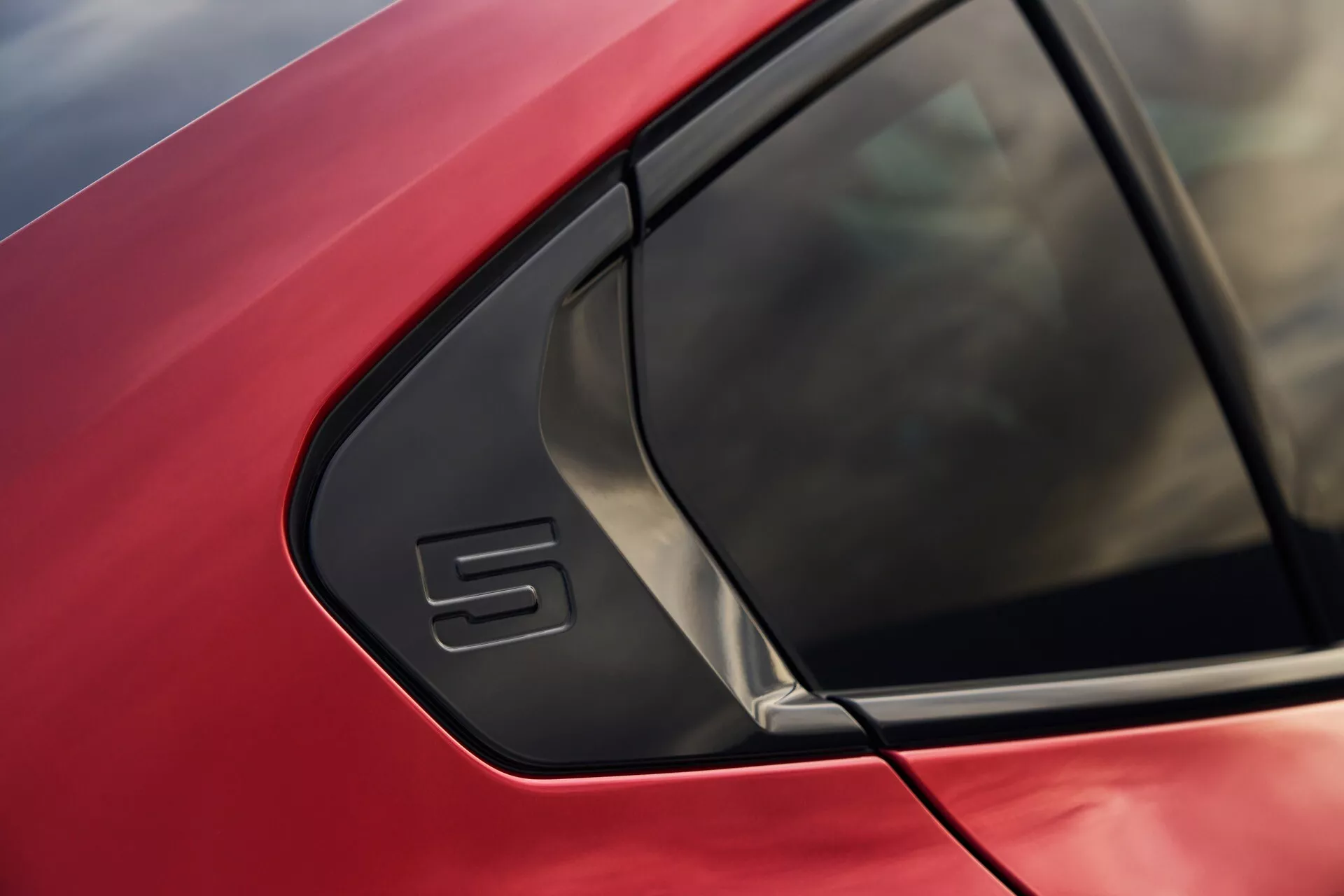 Posnetek iz blizu rdečega avtomobila BMW serije 5 (G60-G61) s poudarkom na območju C-stebrička z značilnim trikotnim oknom in elegantno zasnovo karoserije