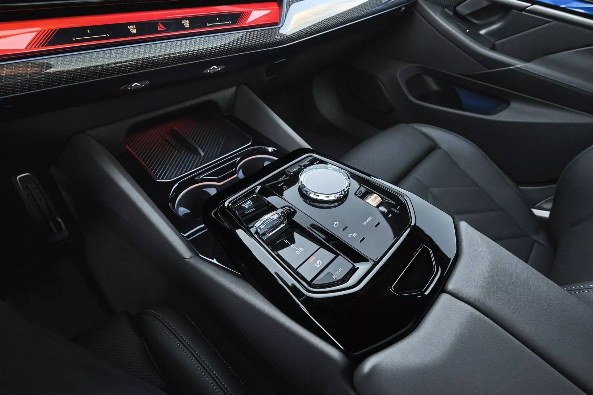 Podroben pogled na sredinsko konzolo BMW serije 5 (G60-G61) 2023 s samodejnim izbirnikom prestav na gumb, upravljalno ploščo na dotik za infotainment sistem, luksuznim naslonom za roke iz usnja s kontrastnim šivanjem in ergonomsko razporeditvijo gumbov in stikal za načine vožnje