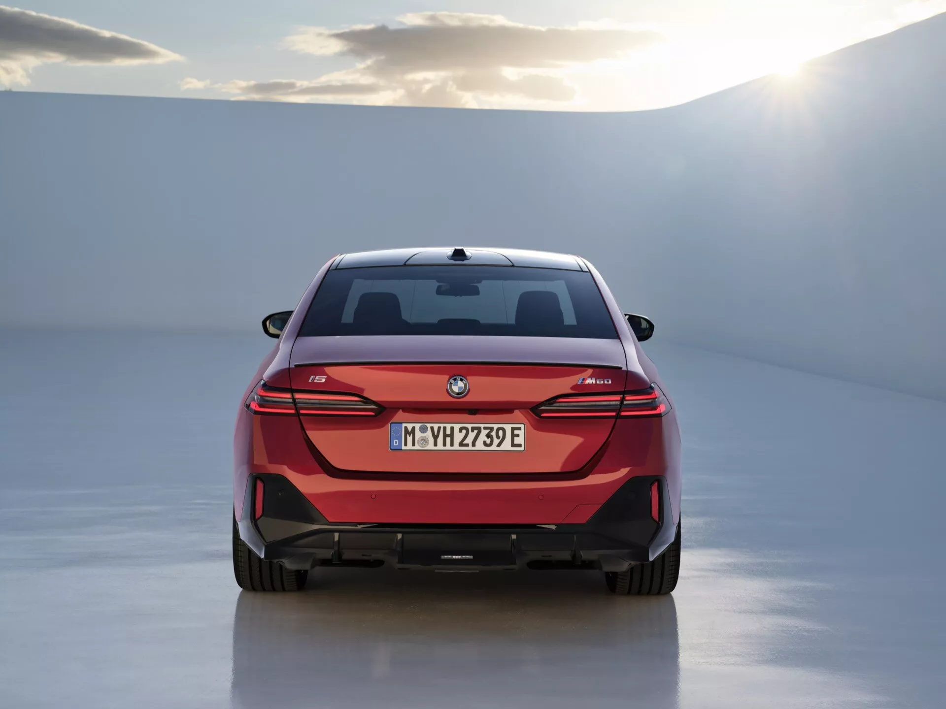 Zadnji pogled na električni avtomobil BMW i4 z LED zadnjimi lučmi, značko tehnologije eDrive in odbijačem v slogu difuzorja, razstavljen v studiu z belim odsevnim tlom in nežno osvetlitvijo.