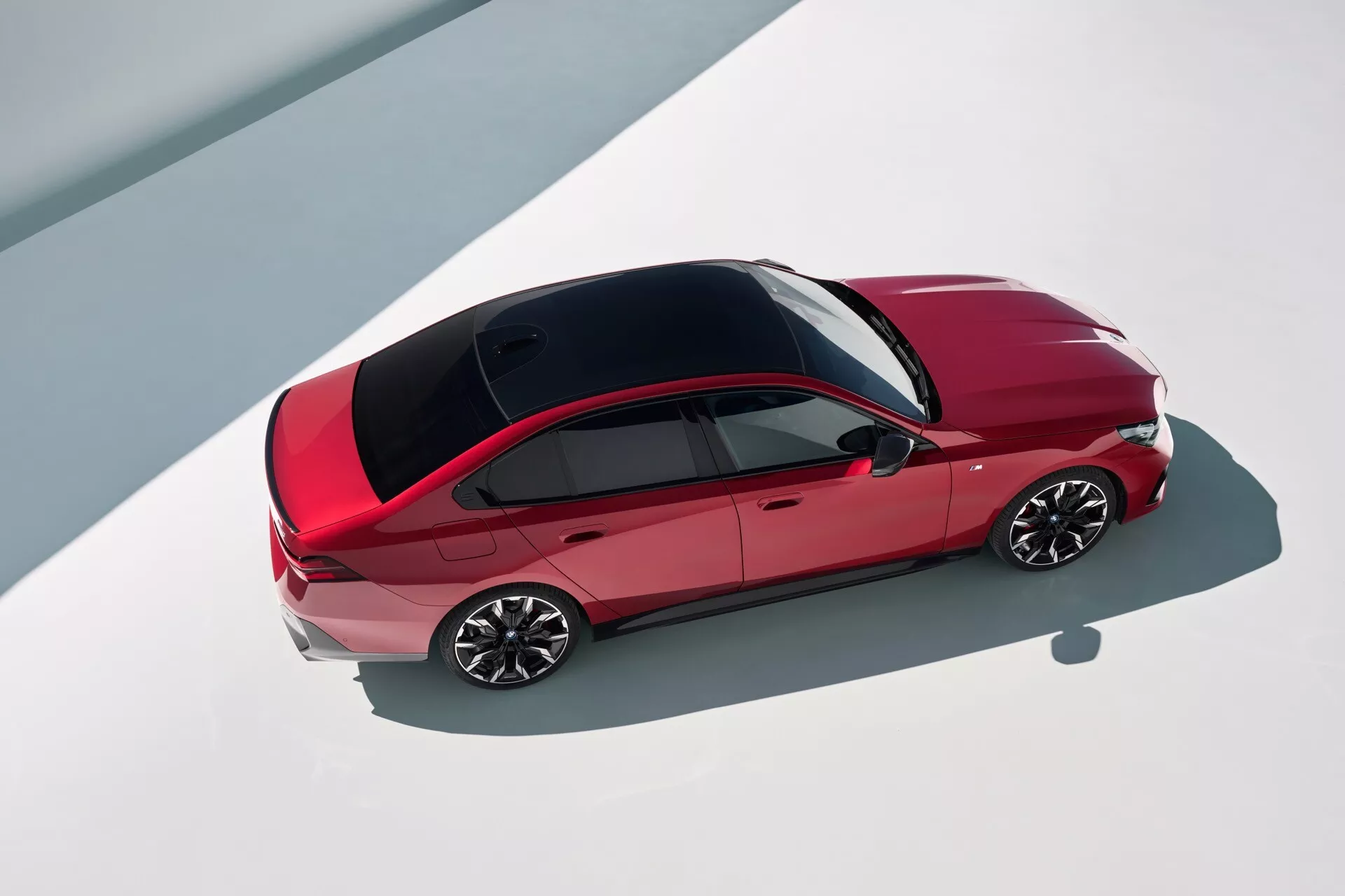 Sedan BMW serije 5 2023 (G60-G61) v rdeči barvi s čistim dizajnom, ki vključuje kontrastno črno streho in večkraka kolesa, pogled od zgoraj, ki poudarja konture vozila na vrhu in estetiko oblikovanja