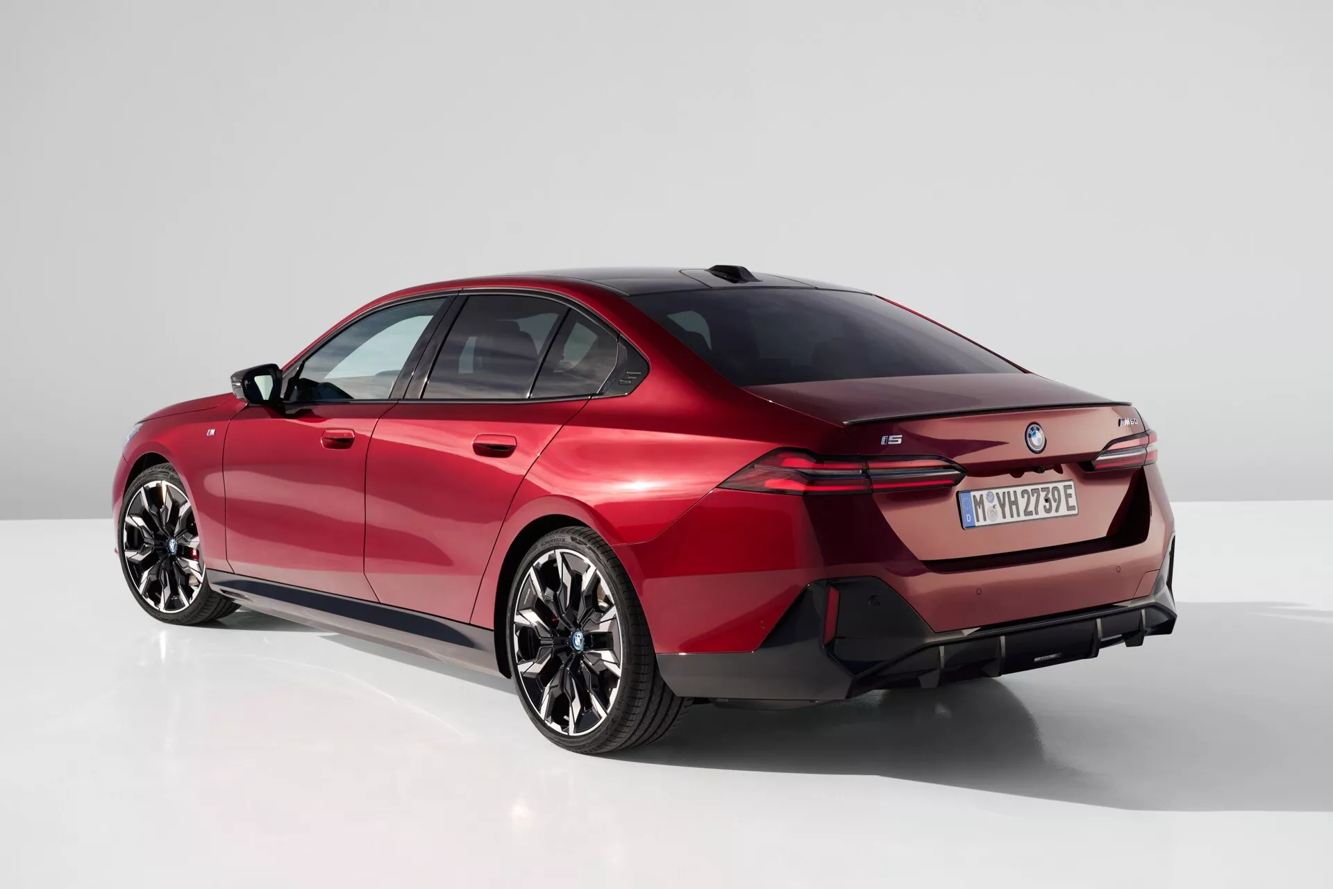 Moderen sedan BMW serije 5 (G60-G61) leta 2023 v studijskem okolju, pogled od zadaj tri četrtine poudarja elegantno linijo strehe, značilne zadnje luči in športni aerodinamični profil v živahno rdeči barvi