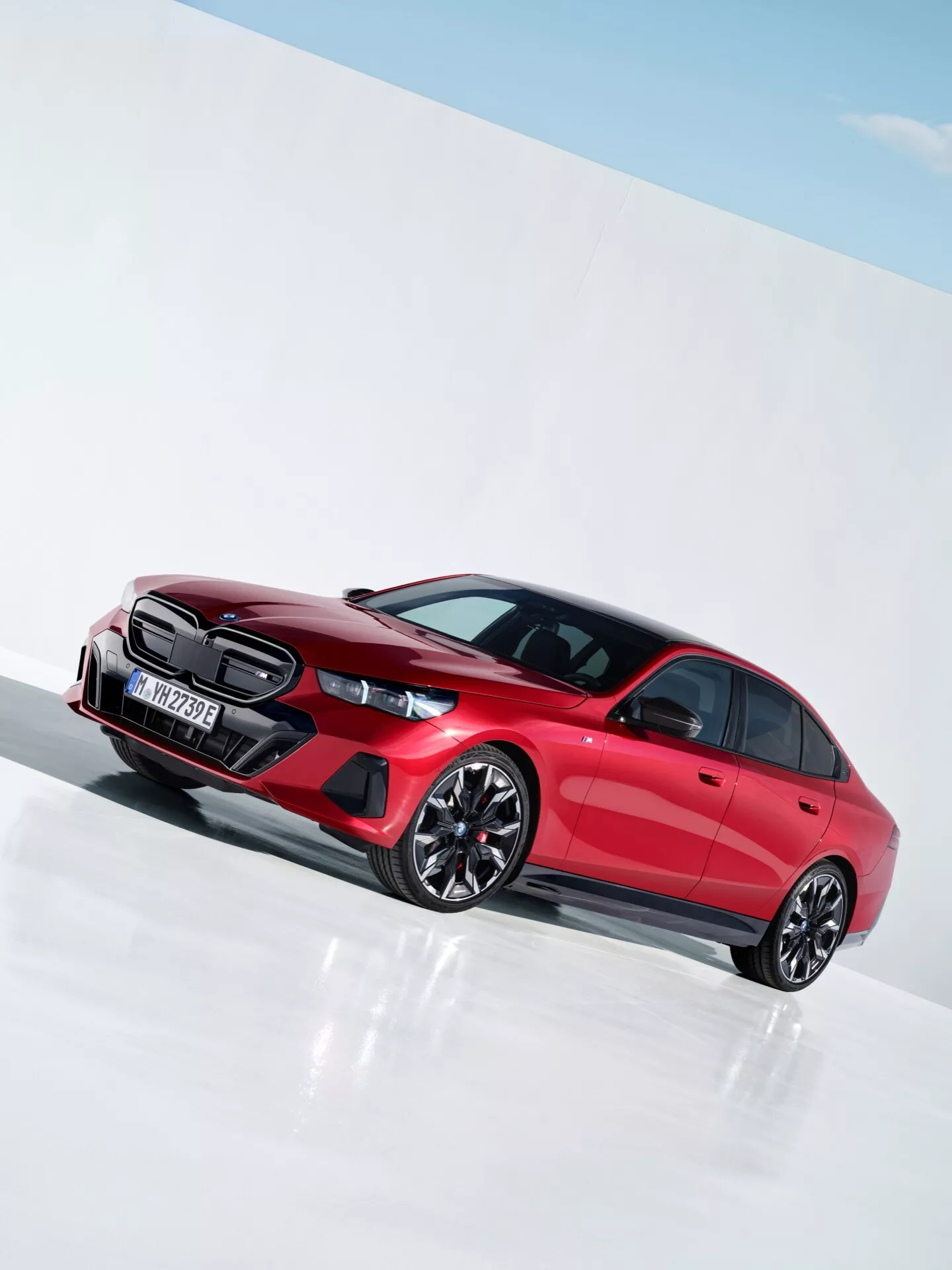 BMW serije 5 letnik 2023 (G60-G61) v živahni rdeči barvi, ki prikazuje športni dizajn z izstopajočo masko, LED žarometi, oblikovanimi vrati in večkrakimi zlitinskimi kolesi v svetlem studijskem okolju