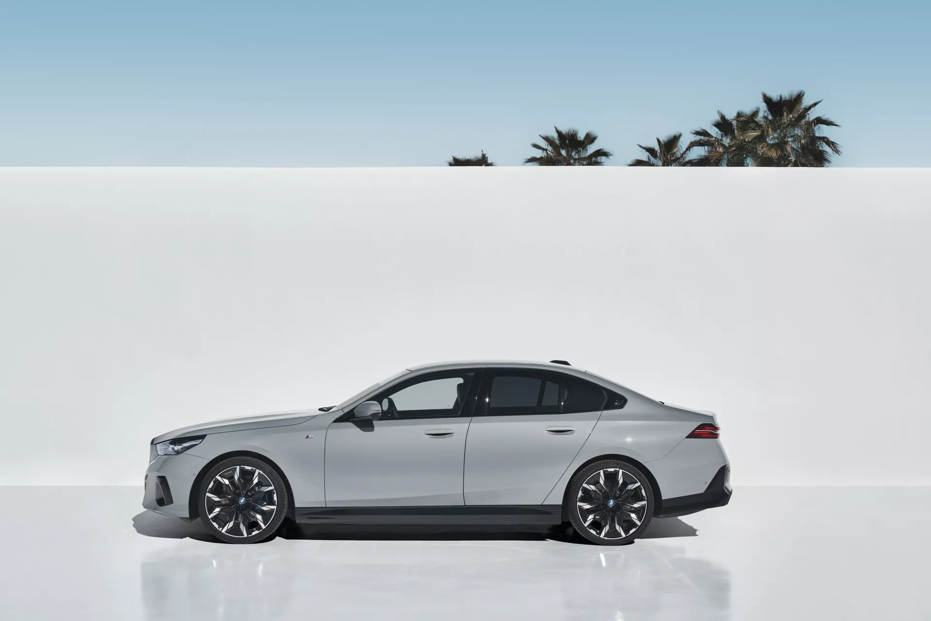Profilni pogled na BMW serije 5 (G60-G61) 2023, ki prikazuje elegantno obliko in športno estetiko z metalik barvo, velikimi zlitinskimi kolesi in aerodinamično silhueto na minimalističnem ozadju z dlanmi