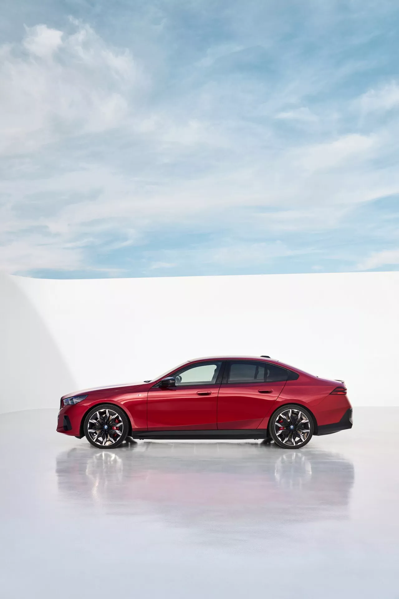 Moderen stranski profil BMW serije 5 (G60-G61) 2023 v živahni rdeči barvi, ki izpostavlja elegantne oblikovalske linije in športna lita kolesa na profesionalnem studijskem belem ozadju